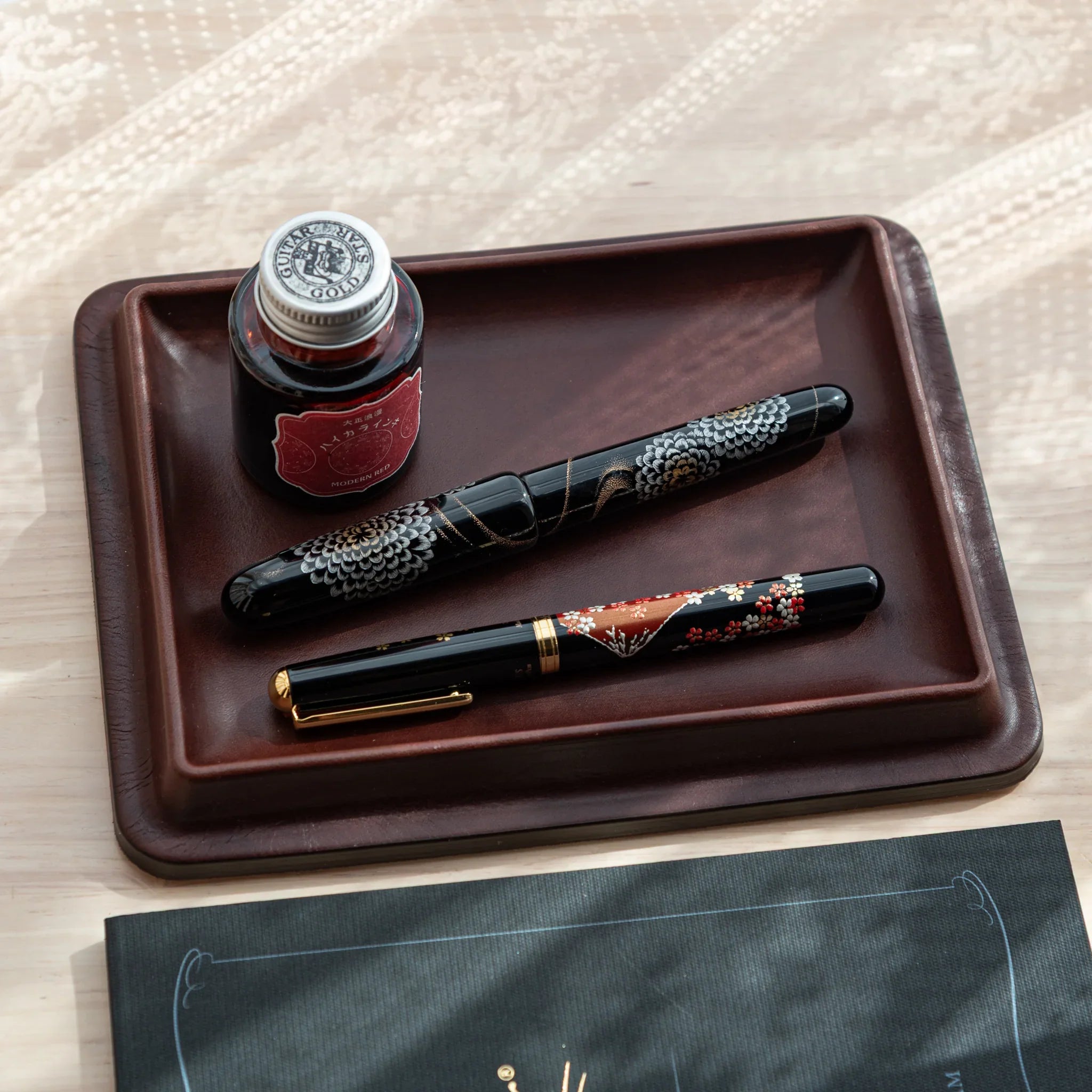 Burgundy wide leather pen tray photographed from overhead displaying stored fountain pens and glass ink bottle clearly
