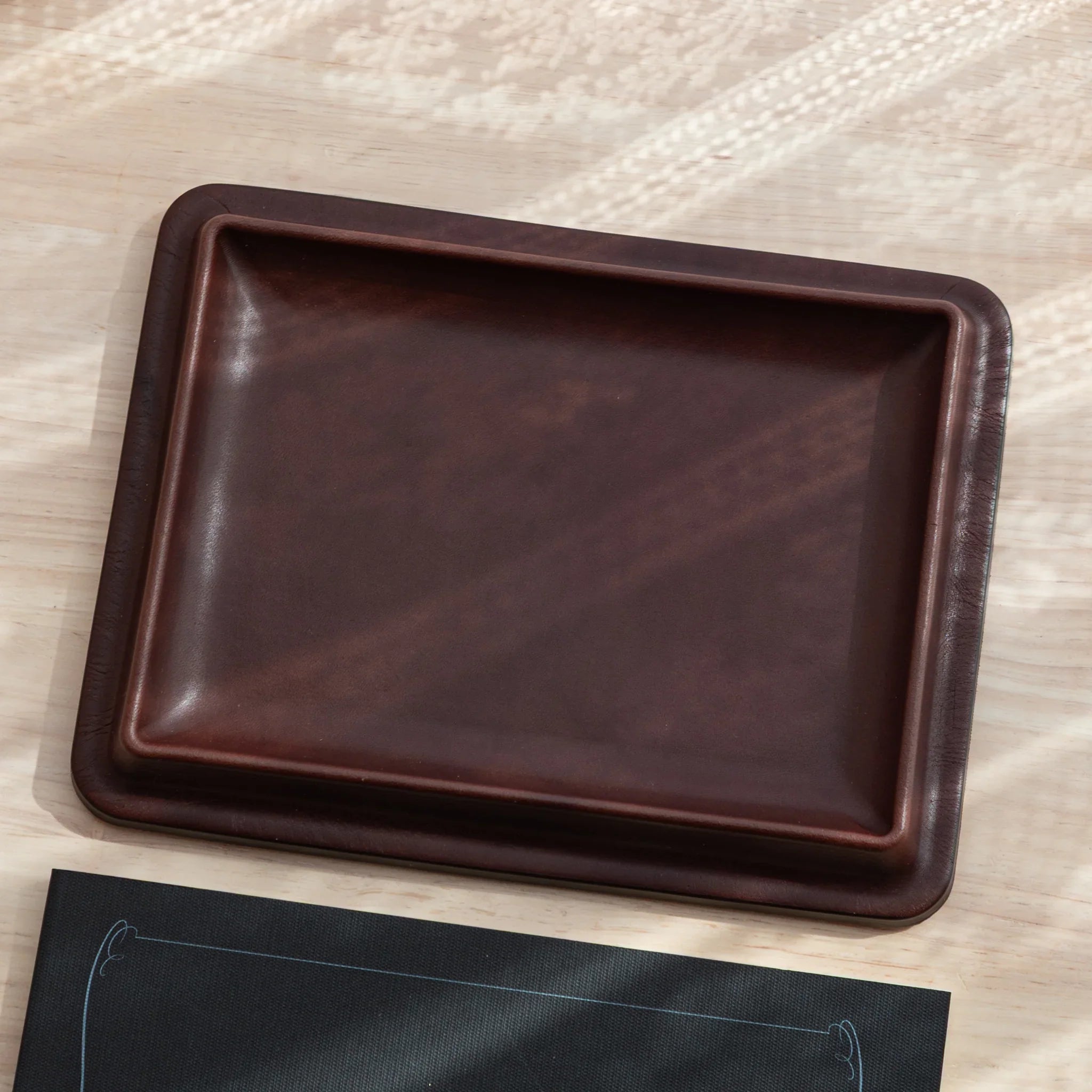 Japanese Pen Tray in tan leather shown empty on light wooden background.