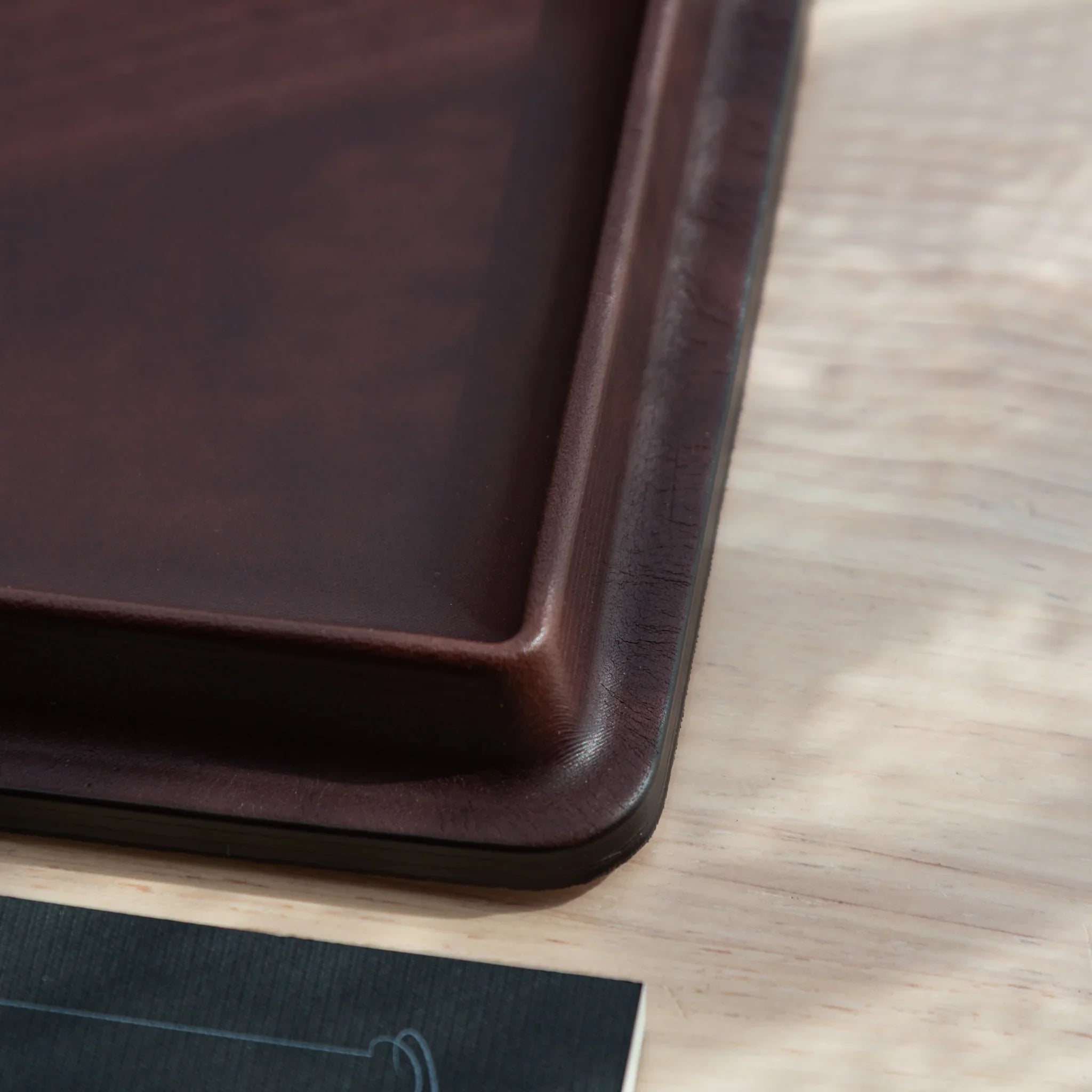 Burgundy wide leather pen tray from side profile highlighting the structured leather construction and curved edge details