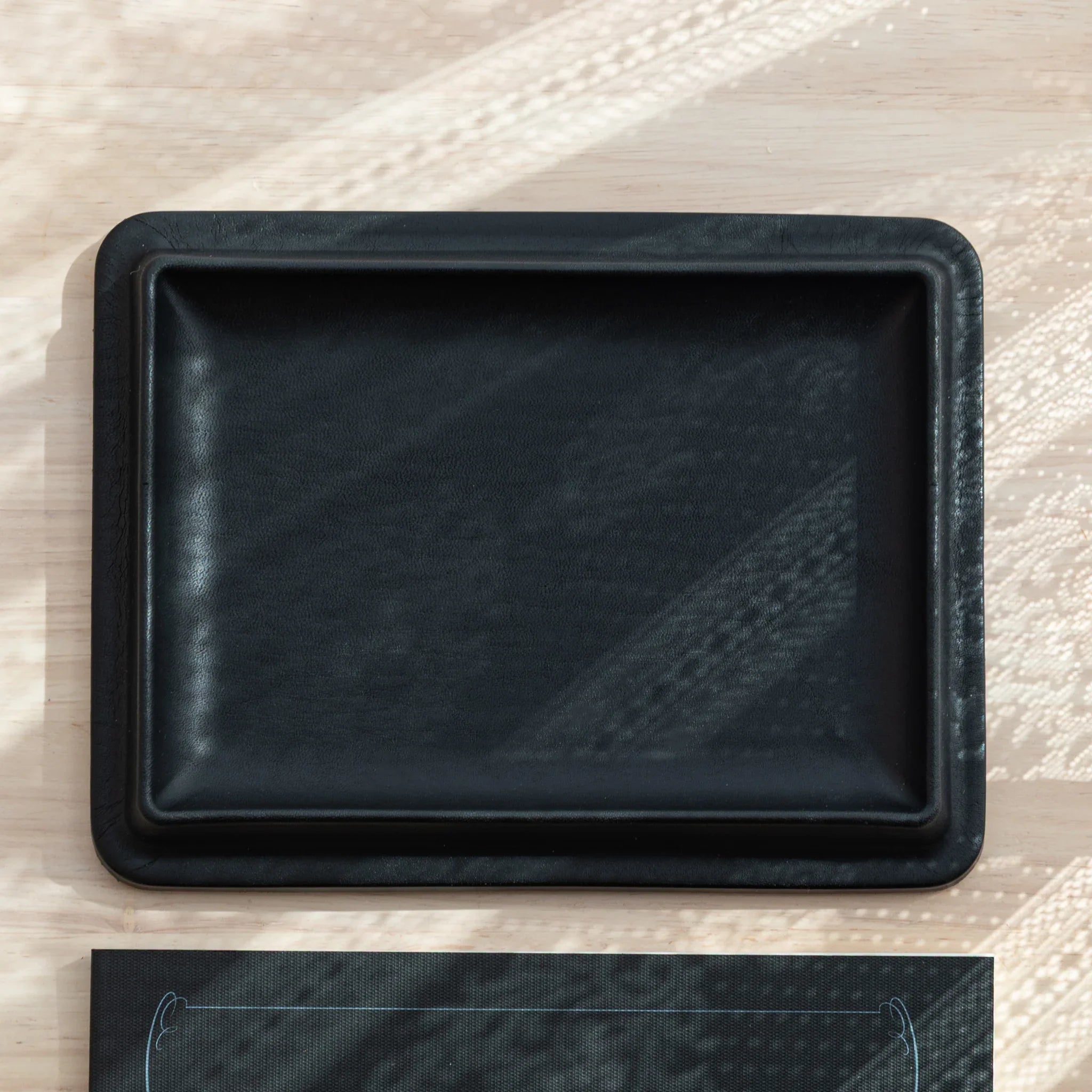 Black wide leather pen tray photographed from side showing the sleek profile, curved edges and finished rim treatment