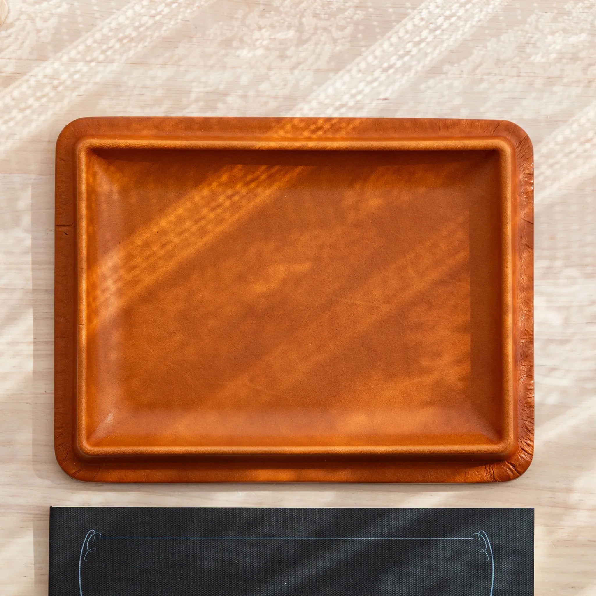 Japanese Pen Tray in camel leather shown empty on light wooden background.