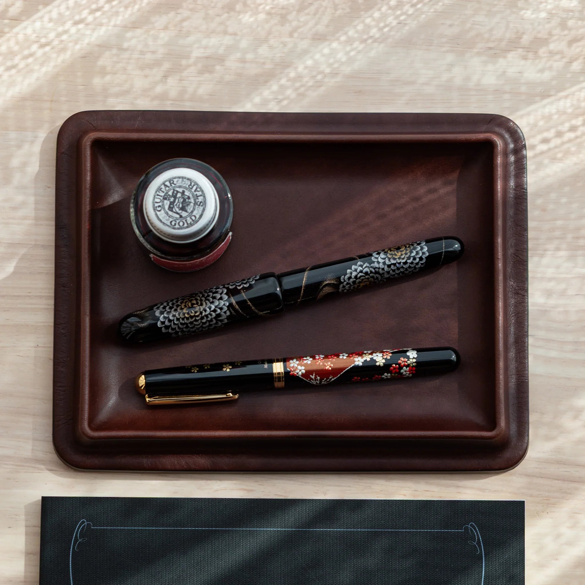 Japanese Pen Tray in tan leather holding brown ink bottle and gold eagle fountain pen.