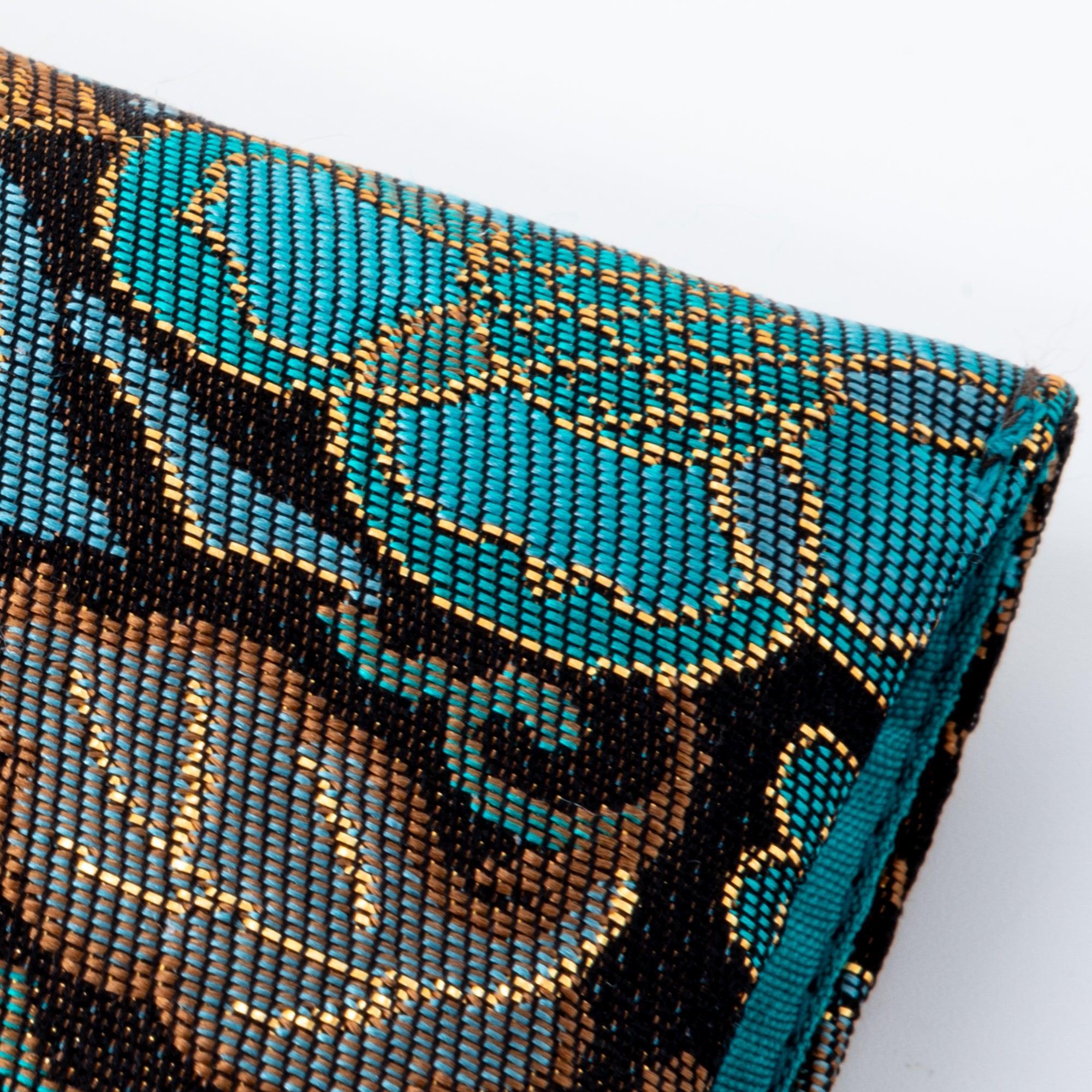 A close-up of a teal and gold Japanese fountain pen case, showcasing intricate floral patterns in Nishijin silk fabric.