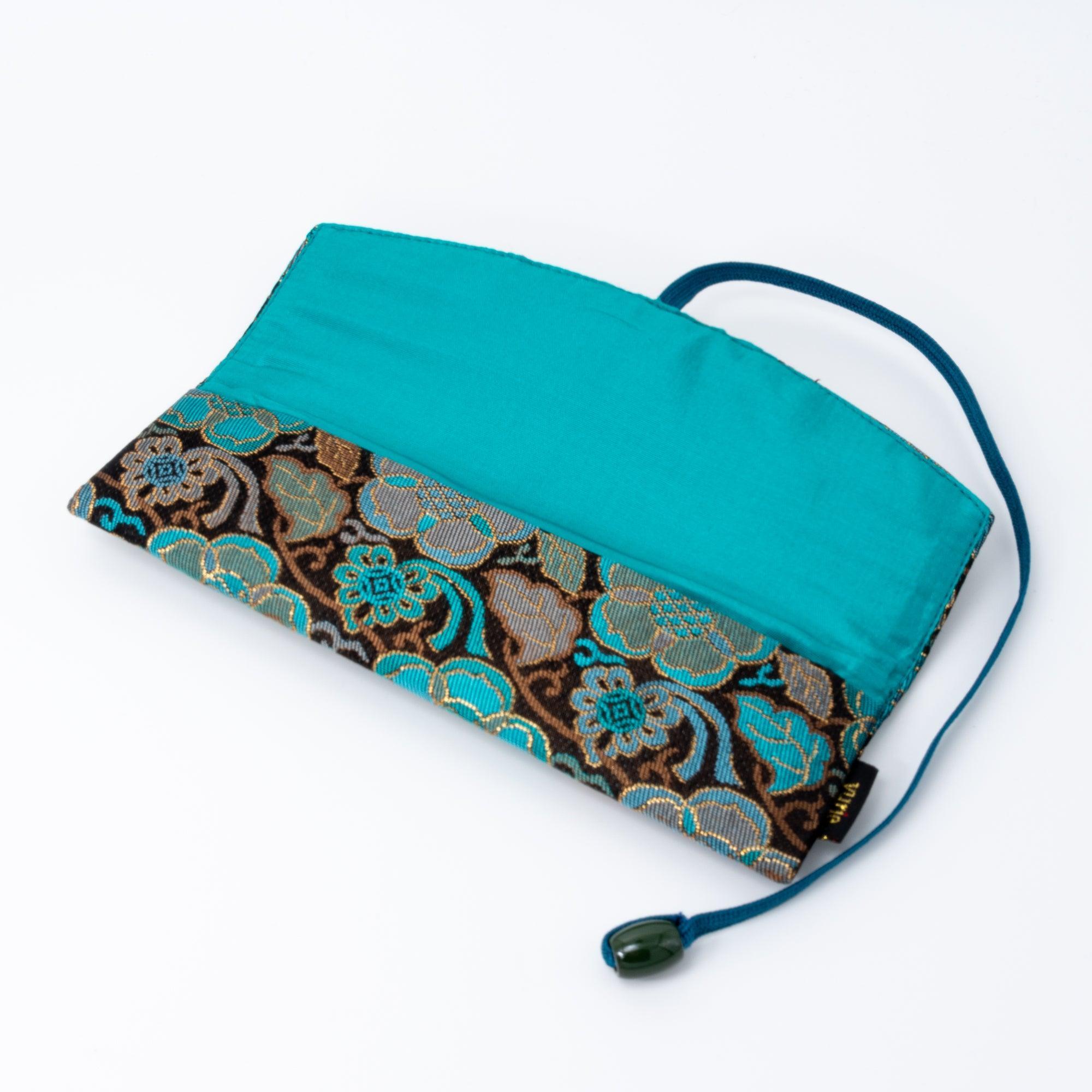 A teal and gold Japanese fountain pen case of Nishijin silk, opened to display its vibrant turquoise fabric lining and blue cord.