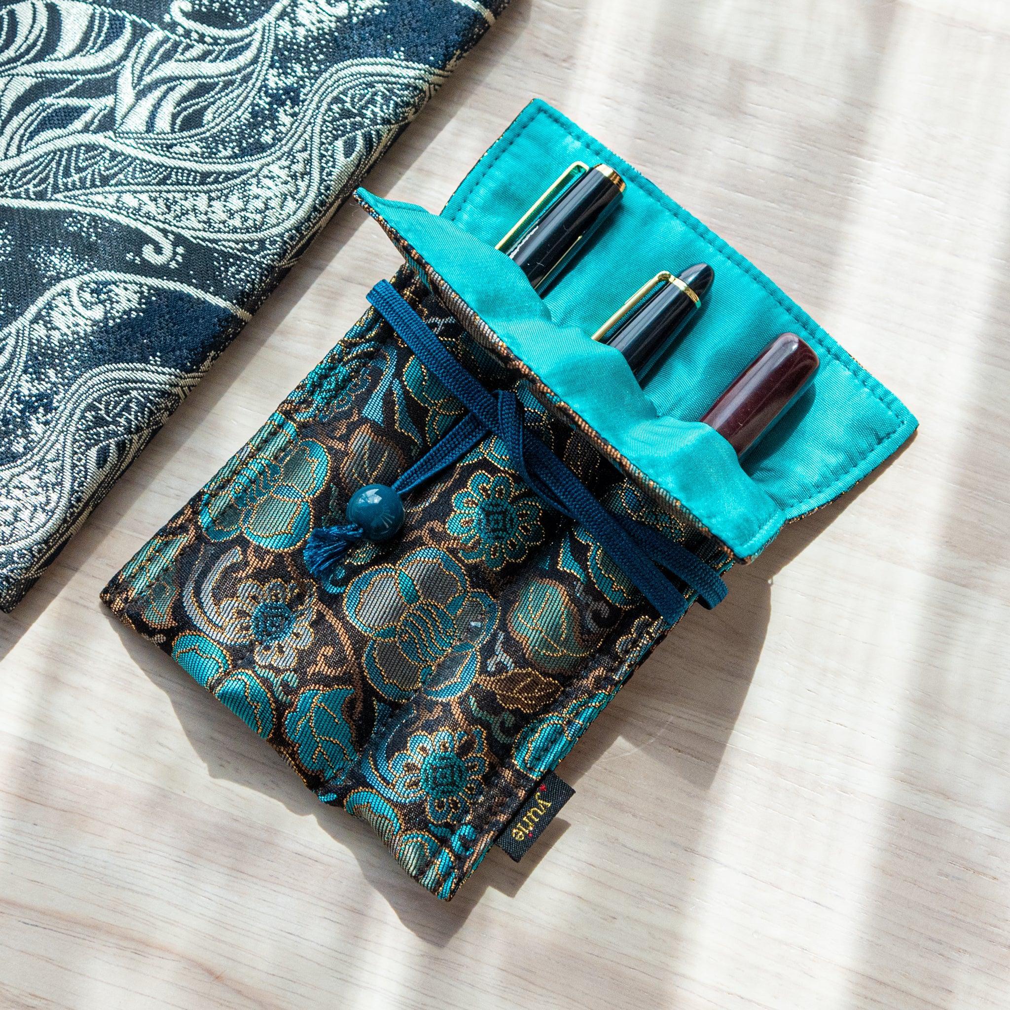 A teal and gold Japanese fountain pen case of Nishijin silk, open to display three fountain pens inside its turquoise fabric lining.