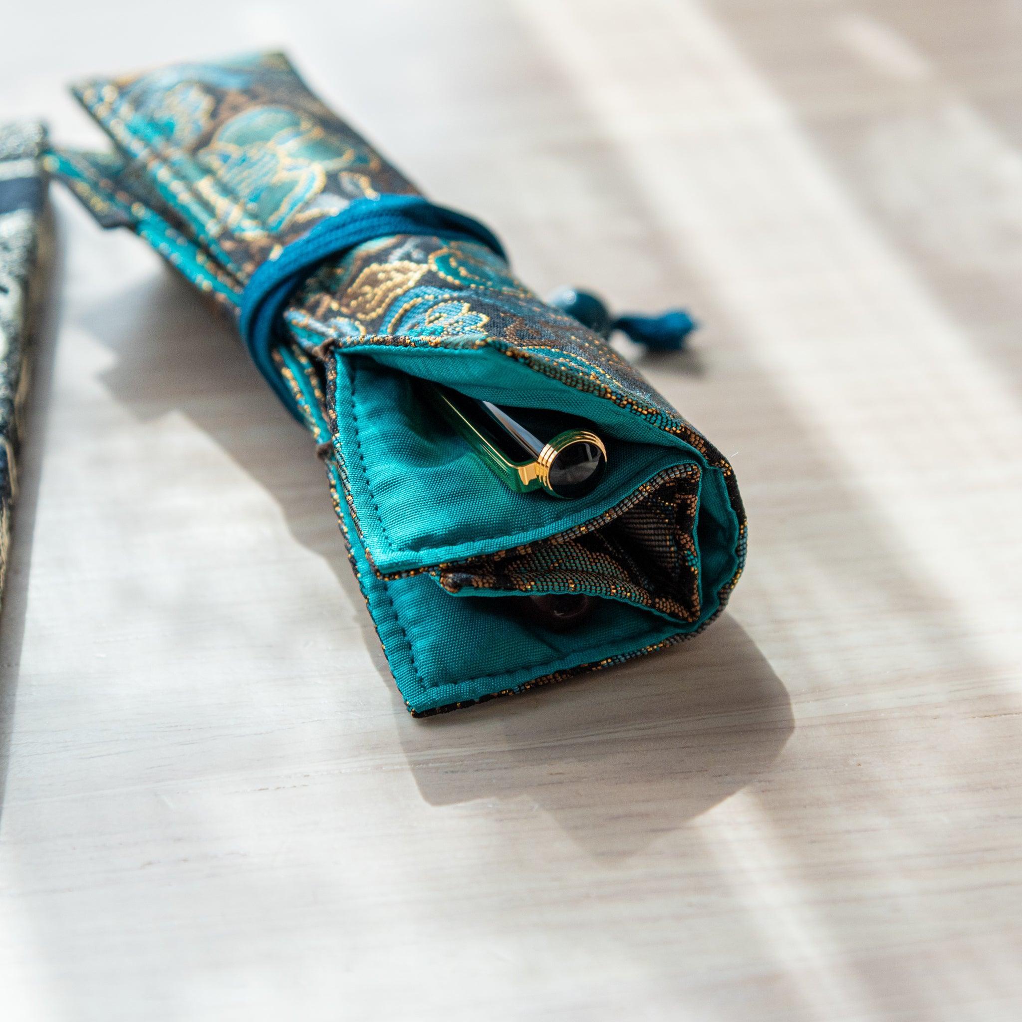 A partially open teal and gold Japanese fountain pen case, showing its turquoise interior and a black fountain pen peeking out.