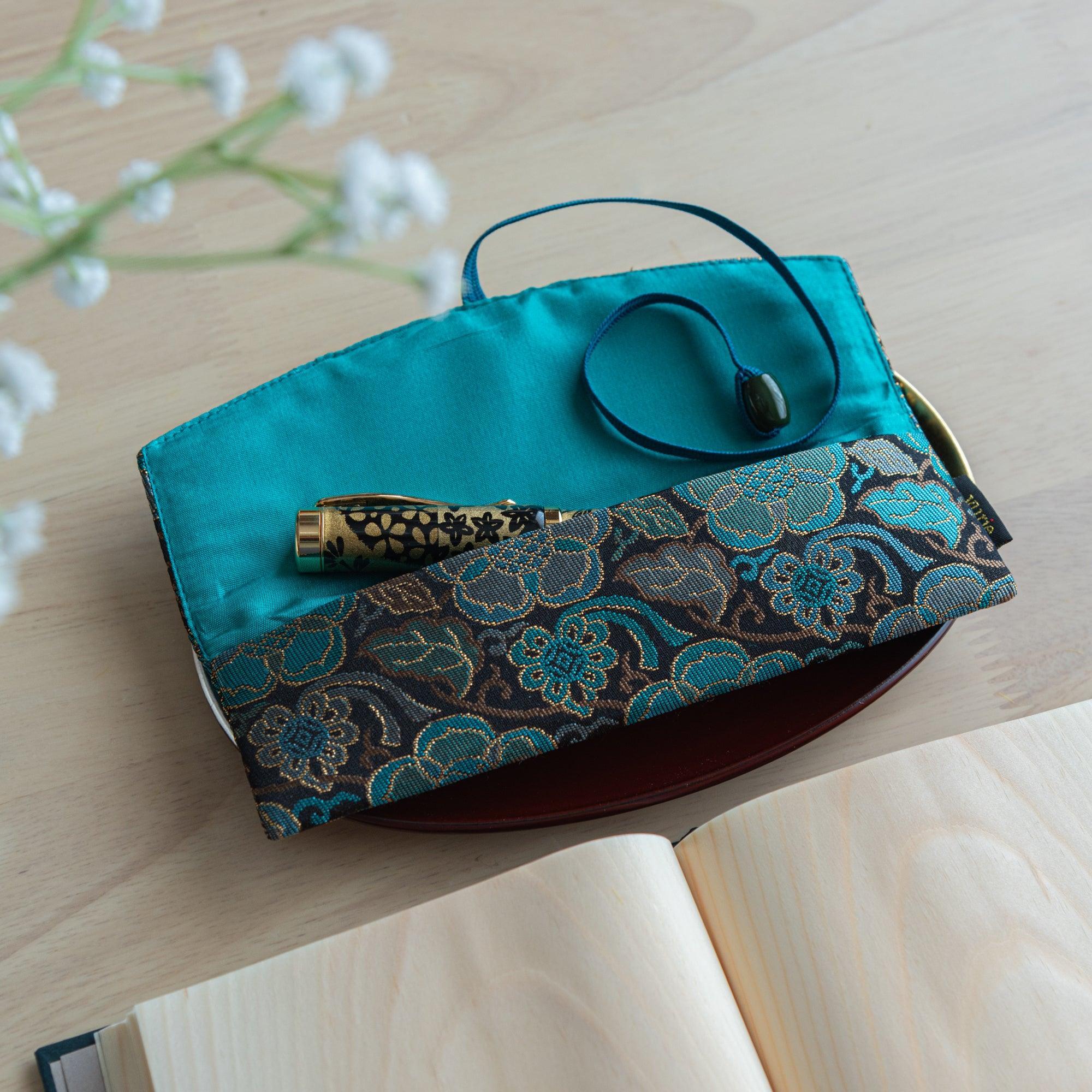 A teal and gold Japanese fountain pen case with turquoise lining, open to display a single ornate fountain pen with gold details.