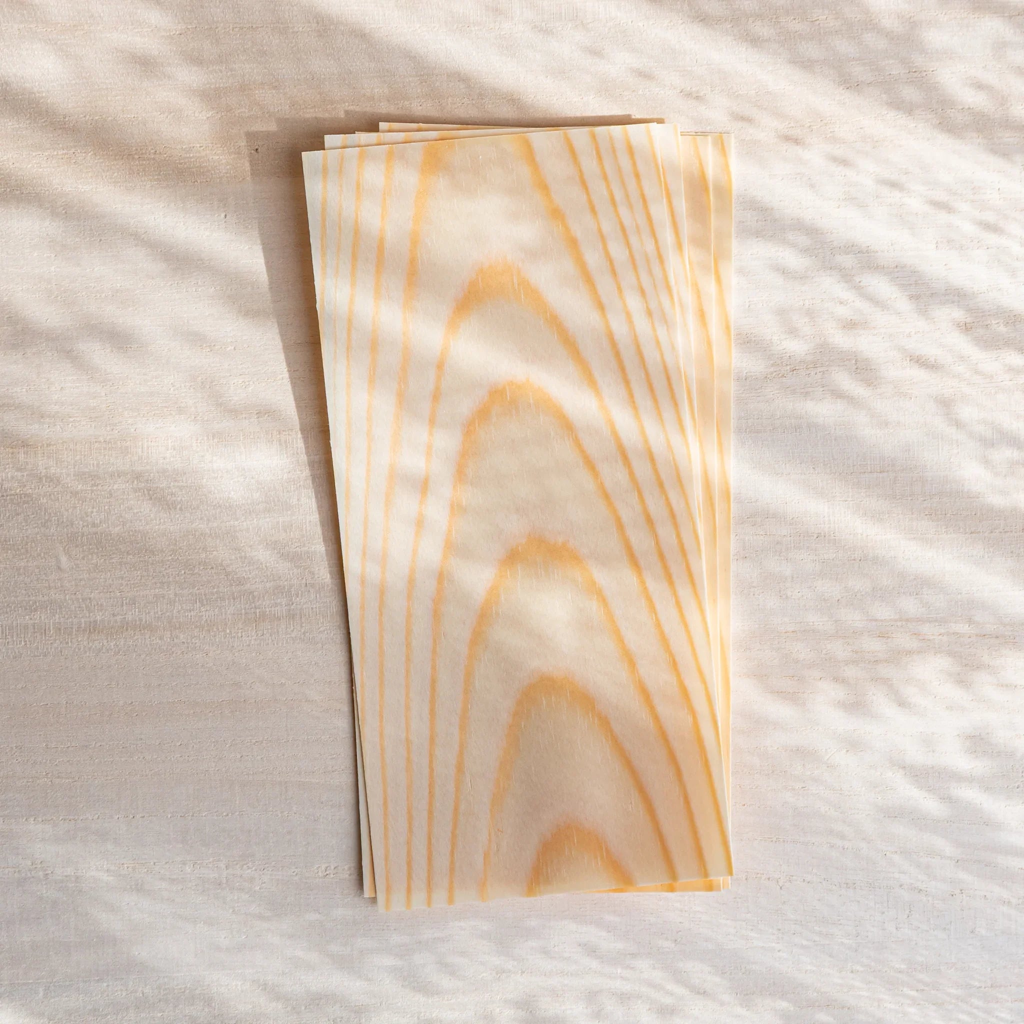 Thin wood message cards stacked on a light desk, with soft curtain shadows highlighting the natural pine grain.