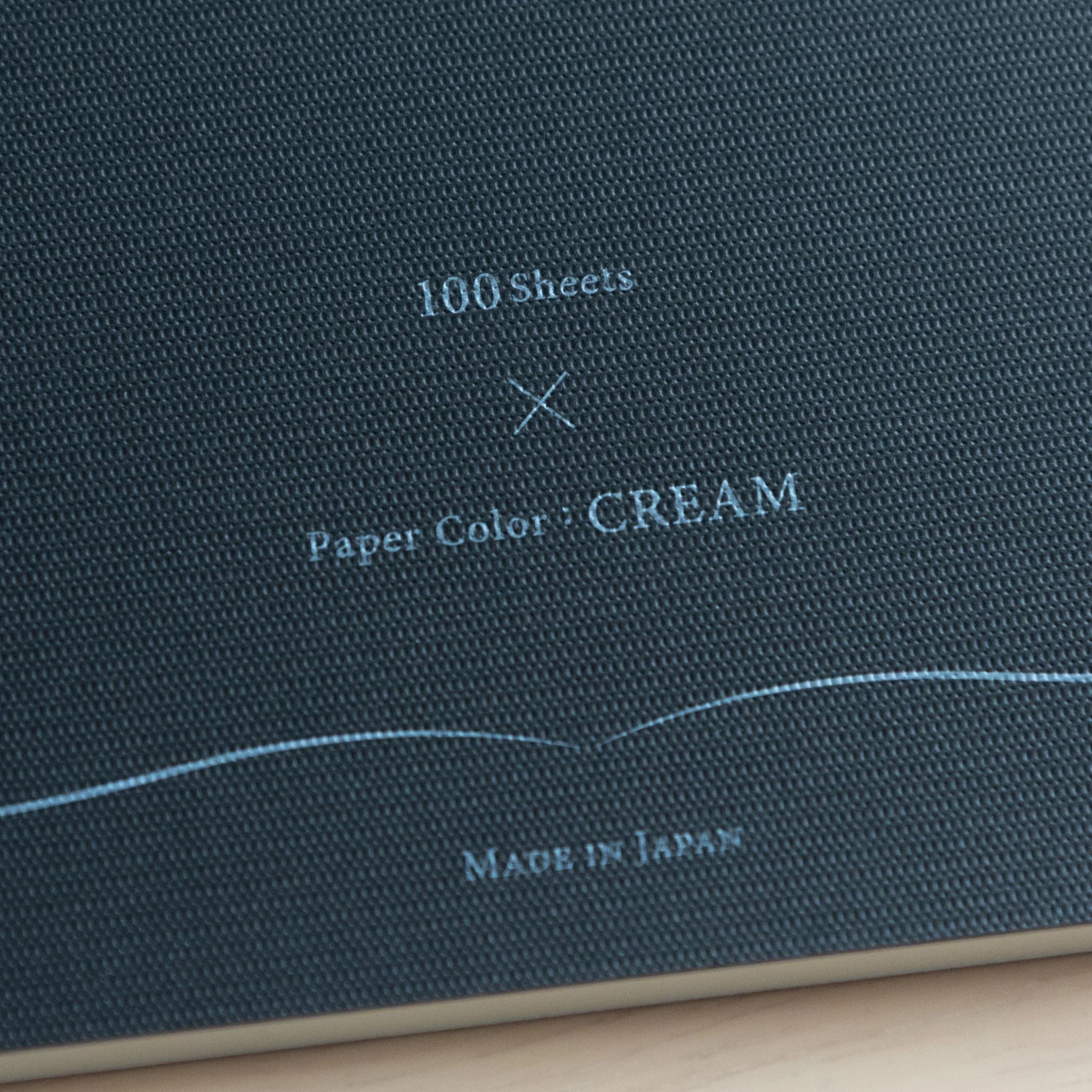 Front cover in deep teal woven textile with embossed gold lettering, curved design elements and page count details