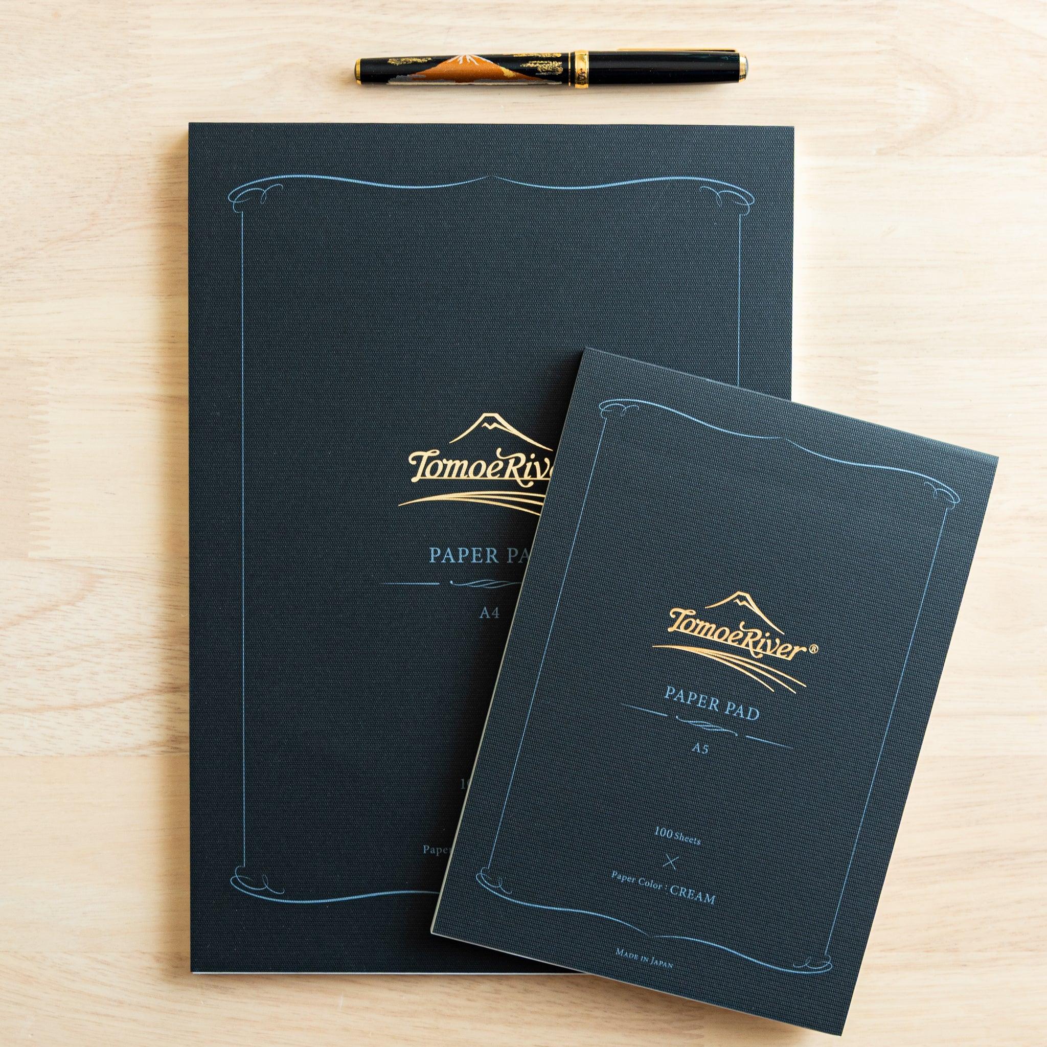 Two writing pads of different sizes styled with fountain pen, teal covers with gold Tomoe River branding