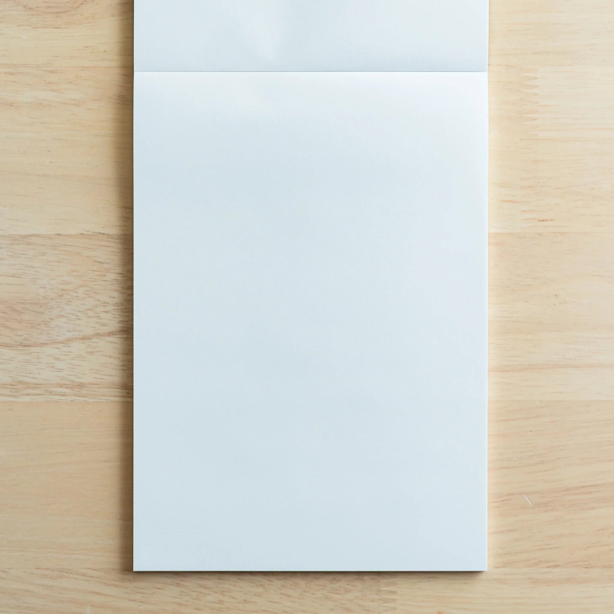 Open writing pad displaying facing blank pages with tan wooden side covers and subtle page divider line at top edge