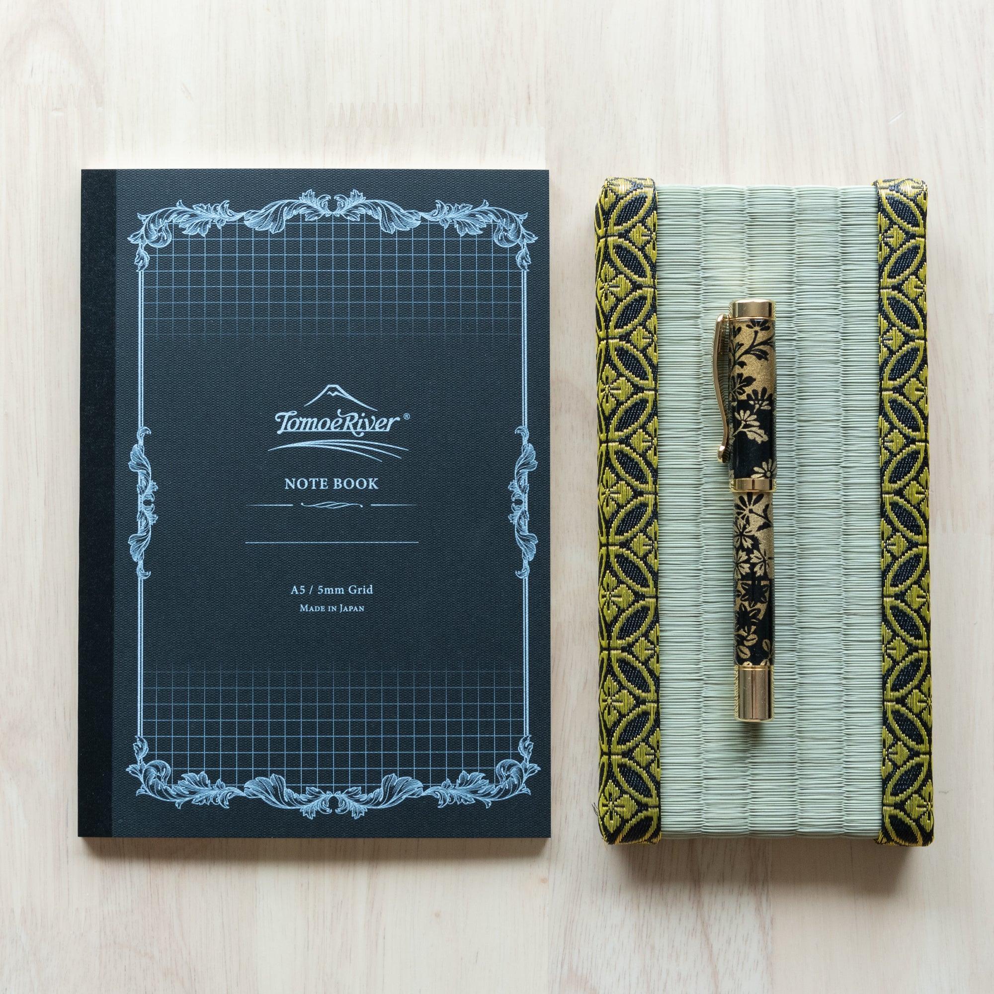 A Tomoe River notebook with a 5mm grid pattern next to a decorative pen case and pen on a wooden surface.
