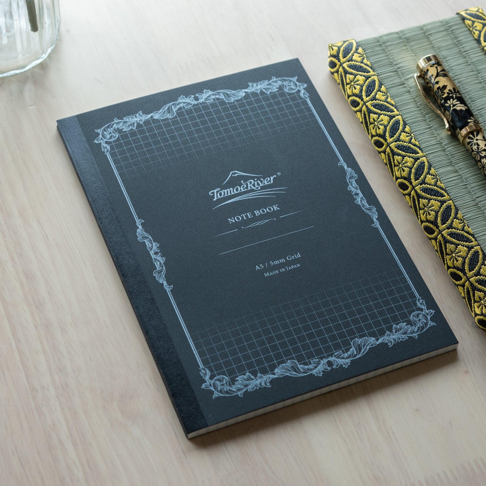 A slightly angled view of the Tomoe River notebook with a 5mm grid pattern, placed beside a patterned pen case and pen.