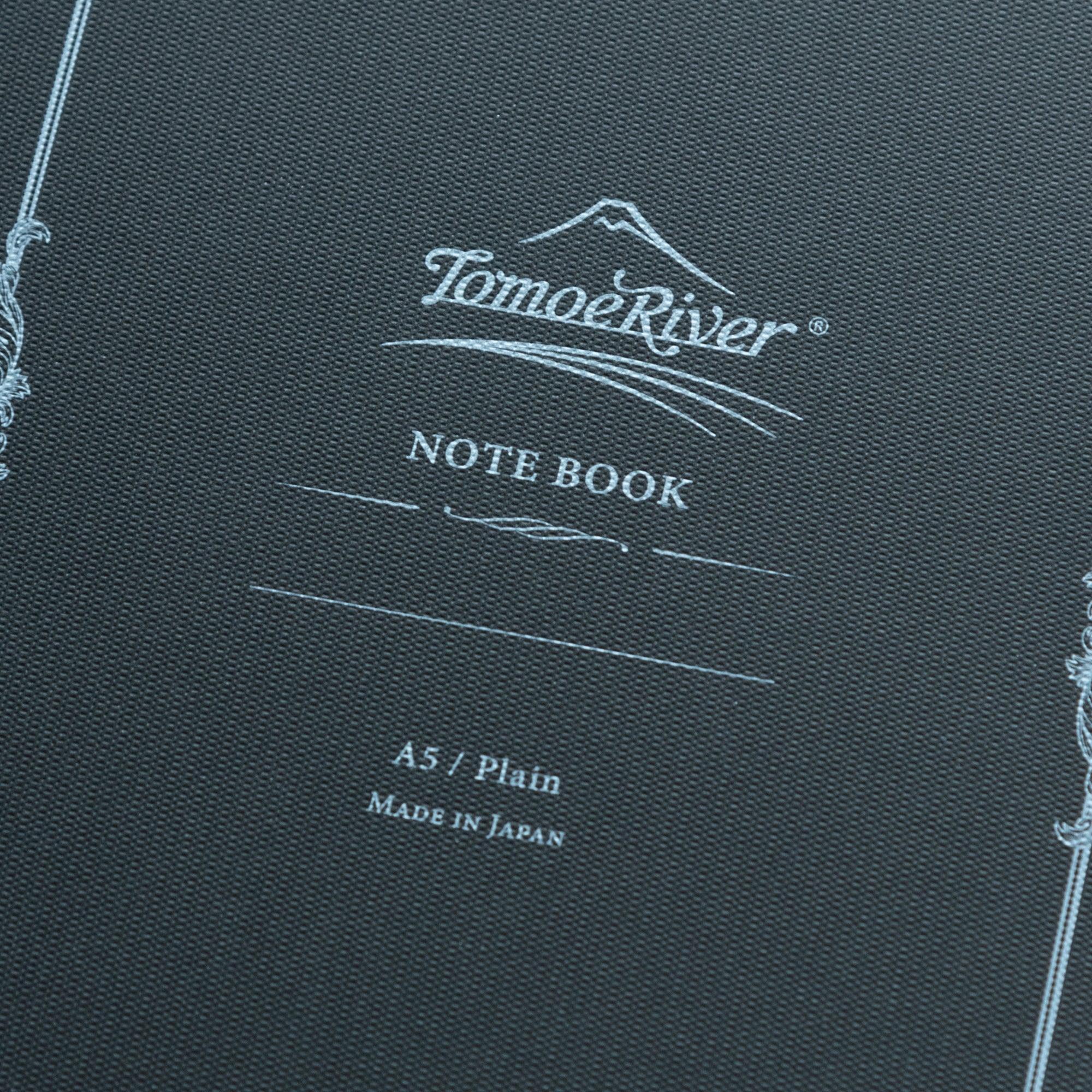 Close-up of the Tomoe River notebook cover, highlighting the logo, decorative border, and "A5 / Plain, Made in Japan" text.