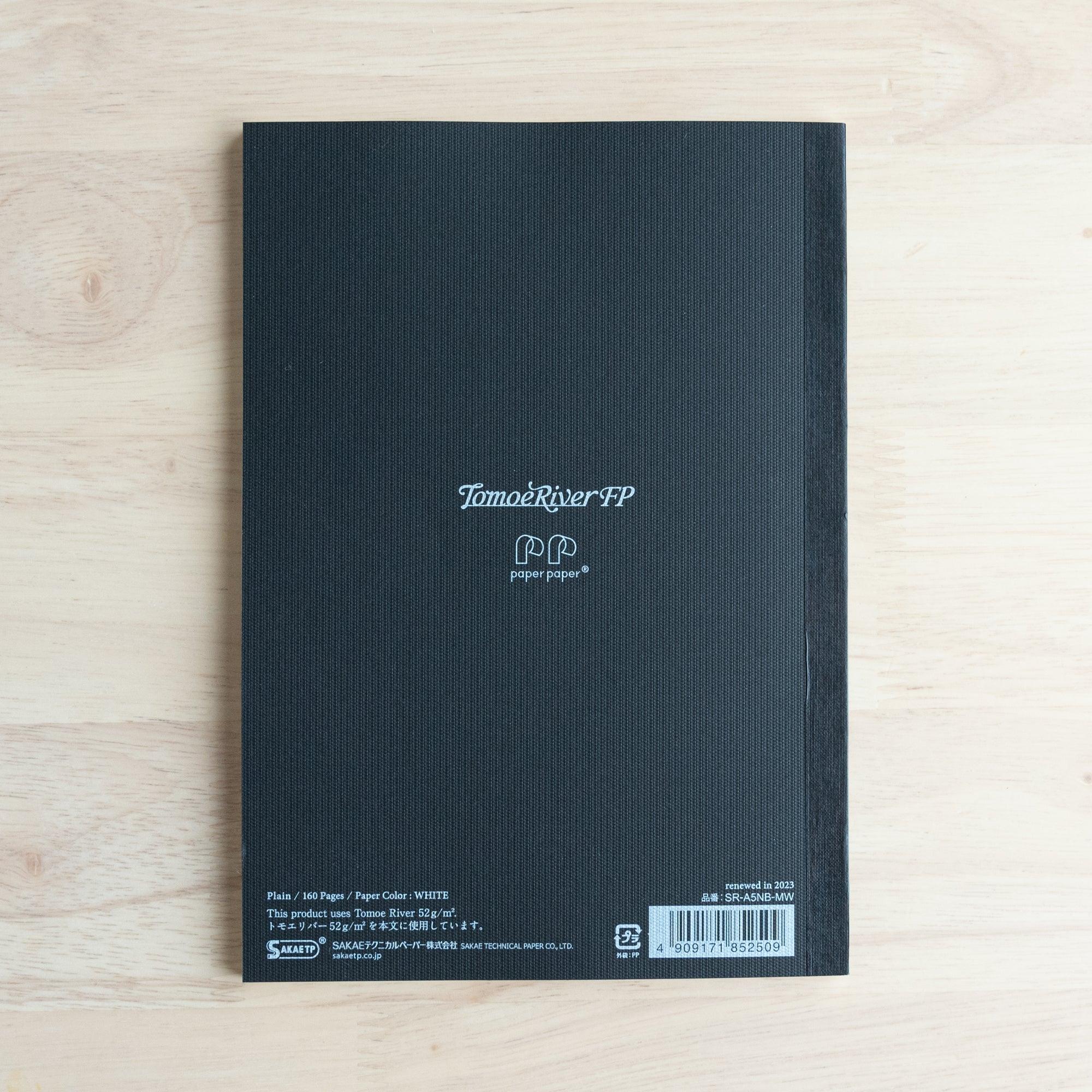 The back cover of a black Tomoe River FP notebook, showing product details, logo, and barcode on a wooden table.