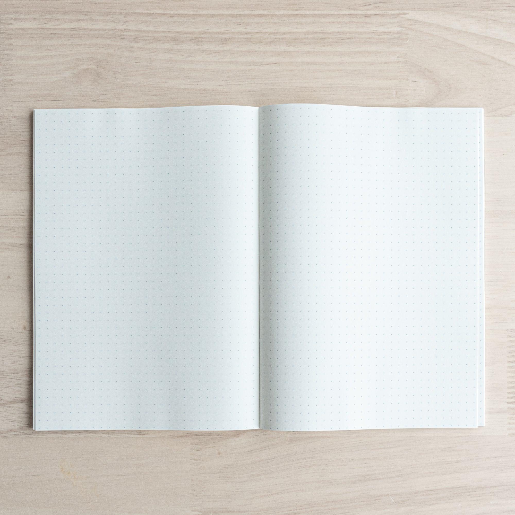 An open Tomoe River notebook on a wooden table, showing blank dot grid pages with evenly spaced dots for writing or drawing.