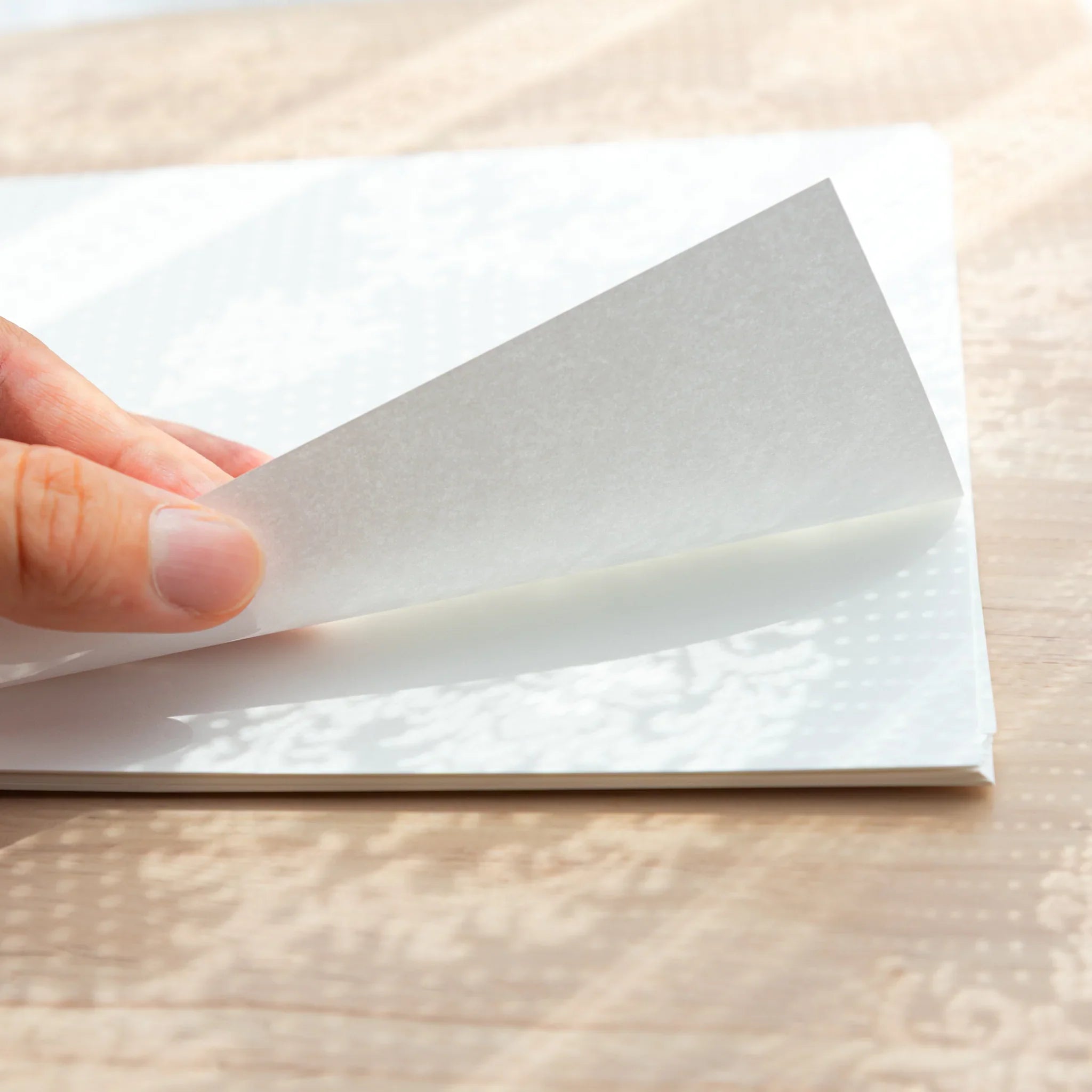 Hand lifting a sheet of Tomoe River White Japanese Loose Leaf Paper A4, showing ultra-thin 52gsm quality.