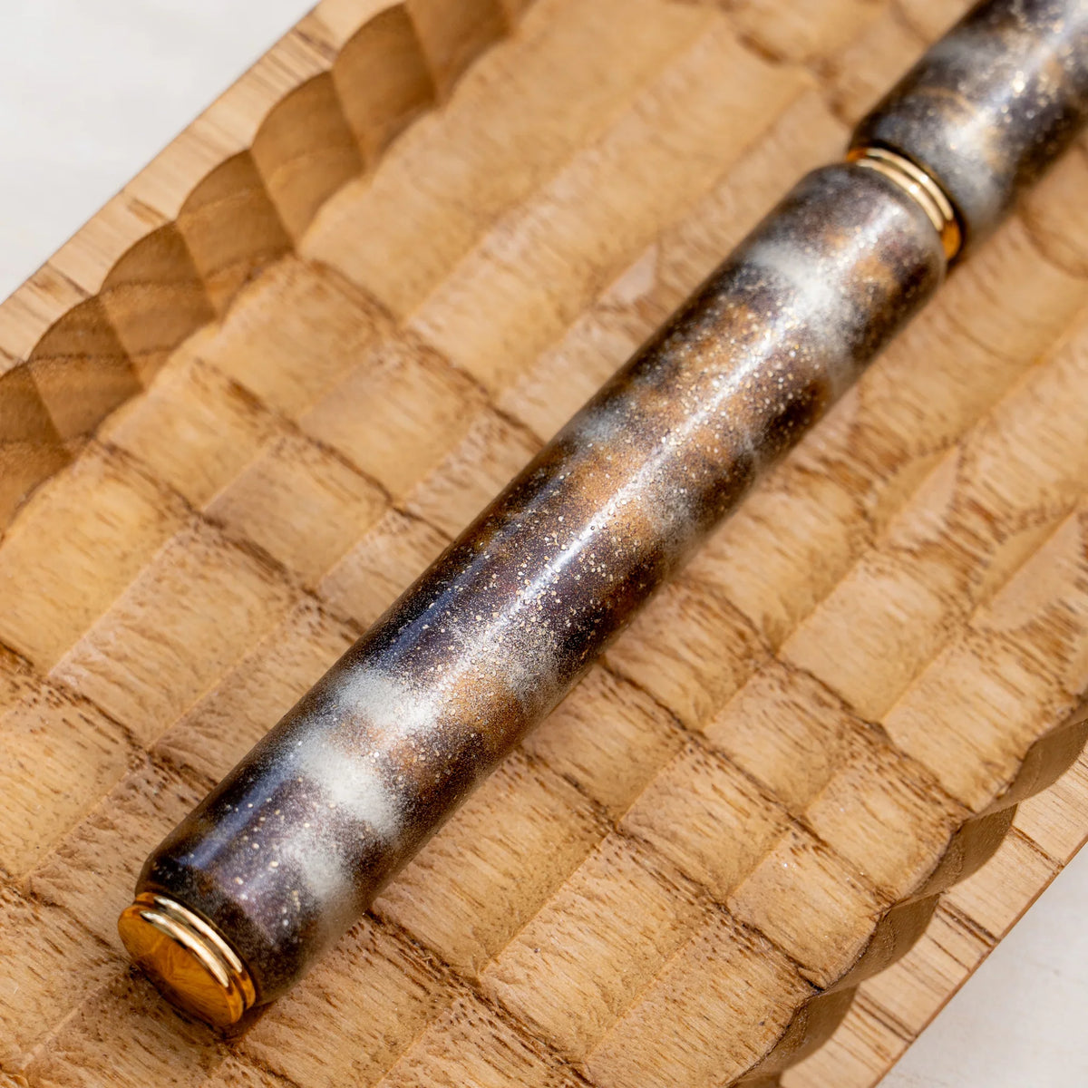 Translucent brown marbled urushi lacquered rollerball pen in zelkova wood, angled view in a carved wooden tray