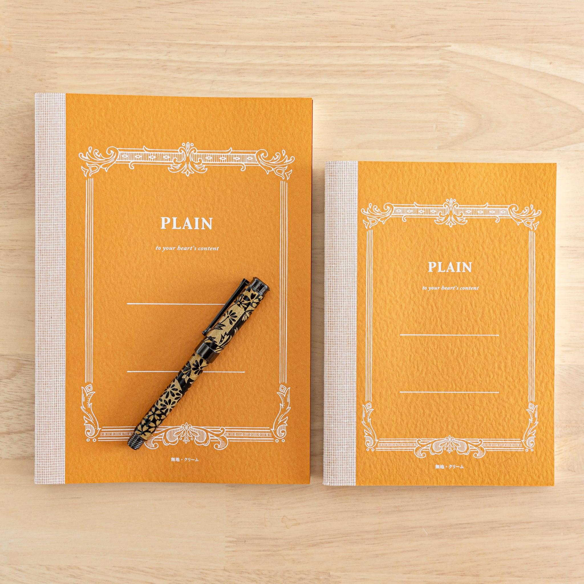 Two orange Tsubame Japanese notebooks labeled "Plain," with a decorative pen on one. Showcasing refined Japanese stationery design.