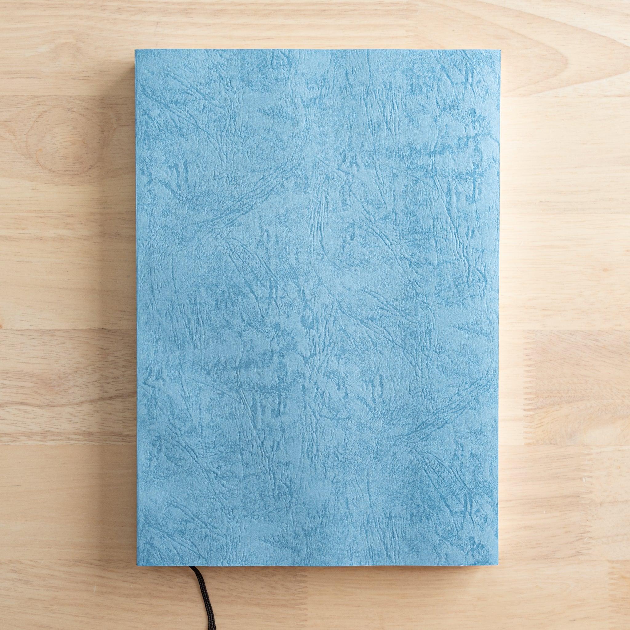 A Japanese notebook with a textured blue cover and a black ribbon bookmark, showcasing high-quality Japanese stationery with an elegant design.