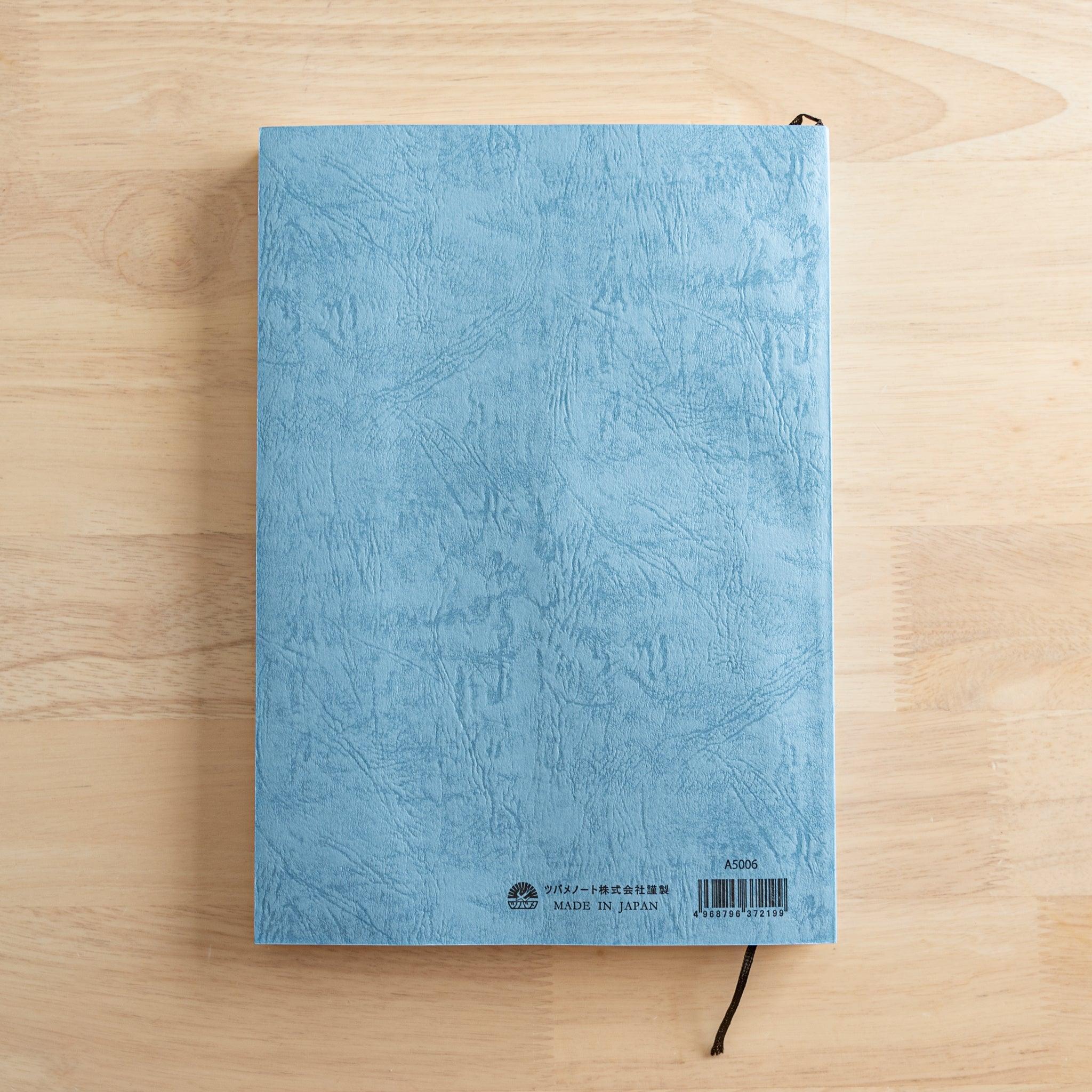 The back cover of a Japanese notebook with a textured blue design, featuring a barcode, brand logo, and "Made in Japan" text, representing fine Japanese stationery.