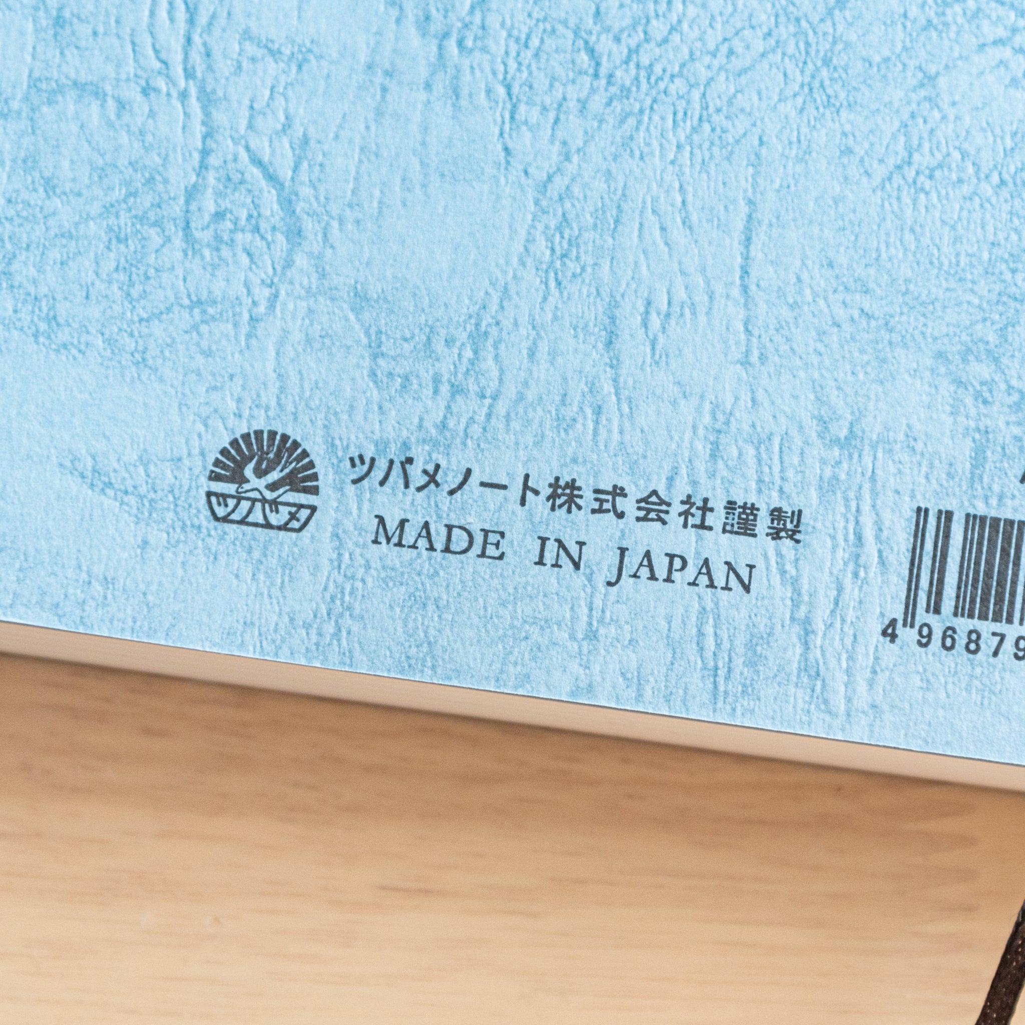The back cover of a Japanese notebook with a textured blue design, featuring a barcode, brand logo, and "Made in Japan" text, representing fine Japanese stationery.
