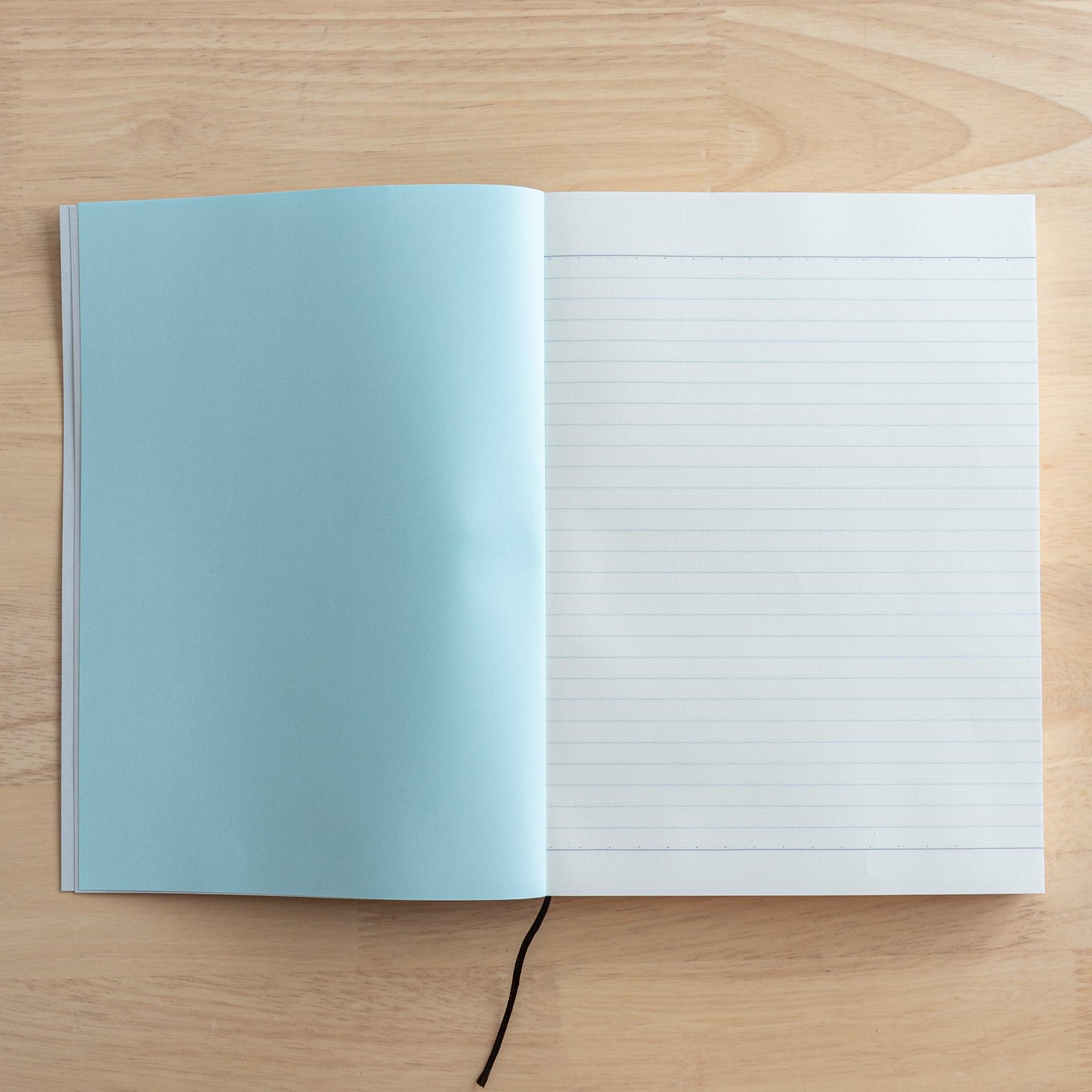 An open Japanese notebook showing a lined page with a light blue inner cover and a black ribbon bookmark, highlighting quality Japanese stationery.