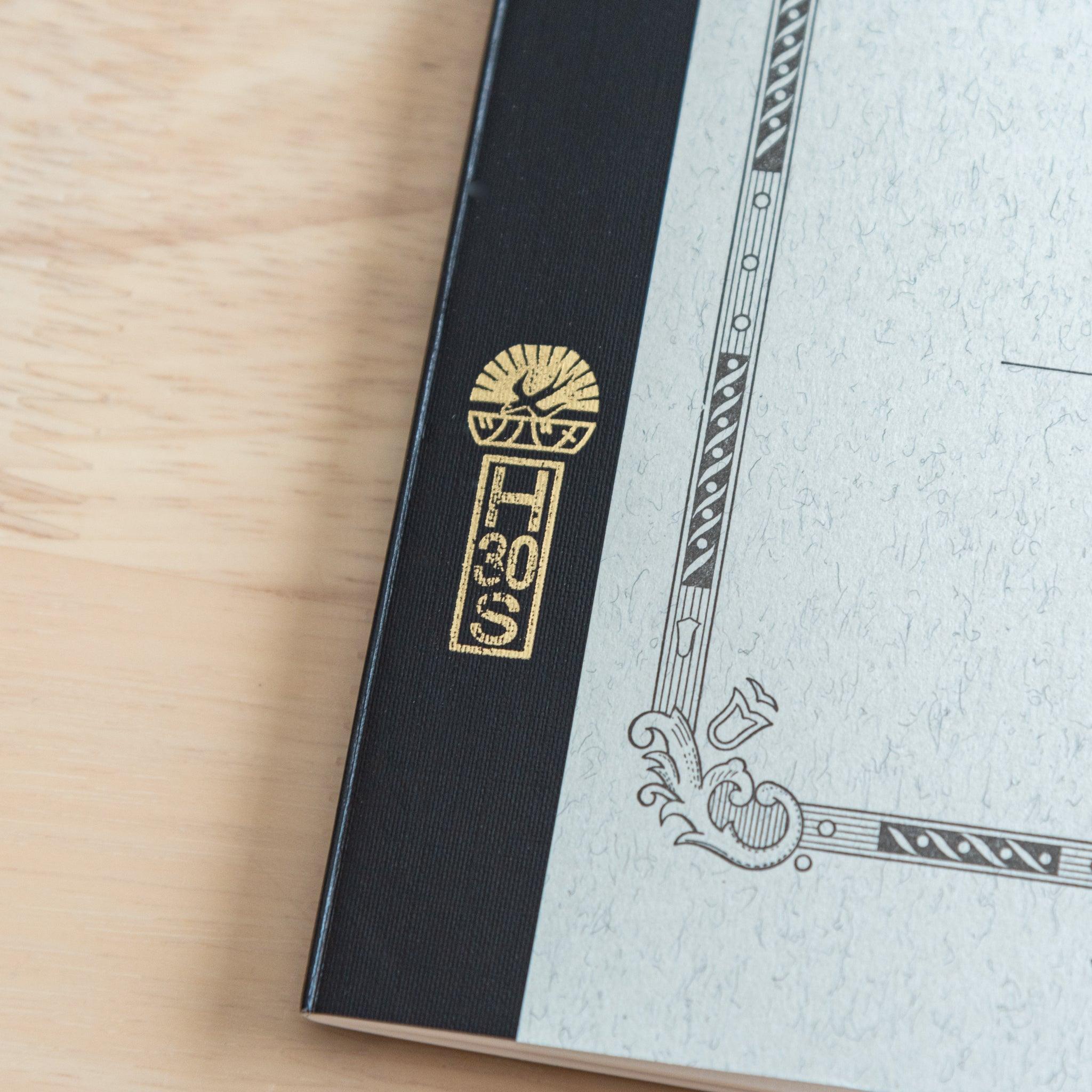 A detailed view of a Tsubame Japanese notebook’s black spine with gold lettering and the brand’s iconic logo, highlighting high-quality Japanese stationery craftsmanship.