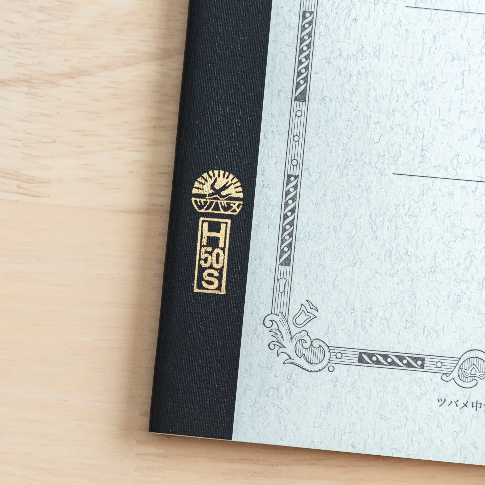 Tsubame Fools University Notebook spine close-up showing gold foil logo on black fabric binding with cream pages