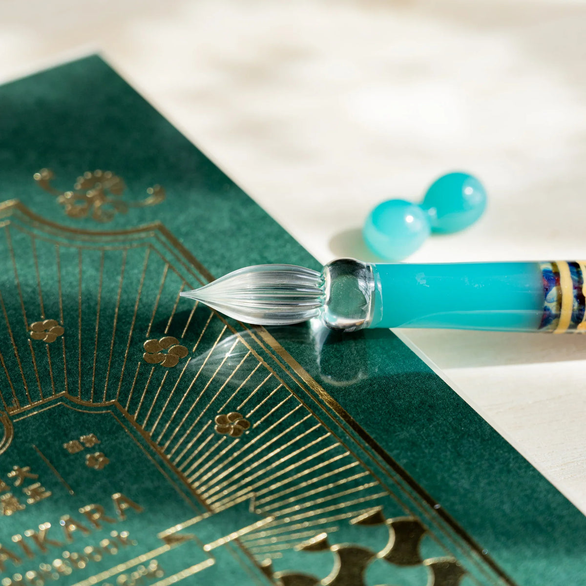 Clear fluted nib of the Turquoise Hemp Leaves pen with a turquoise glass pen rest on a green notebook