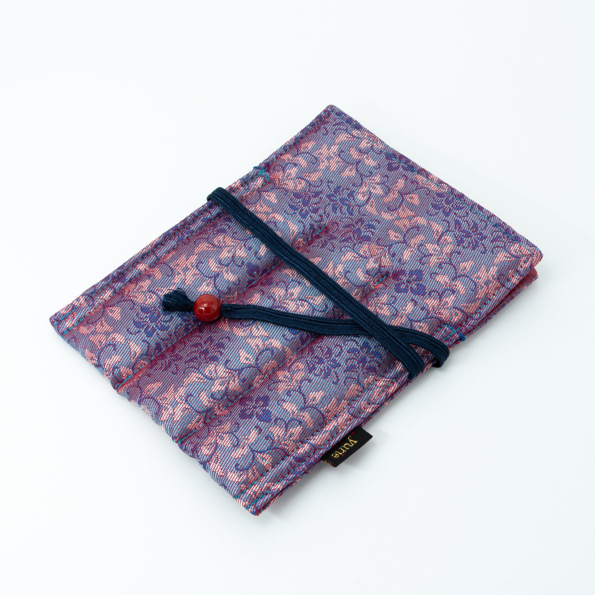 A compact Japanese fountain pen case made of Nishijin silk with pink and blue floral patterns, wrapped with a navy cord and red bead, displayed on a white background.