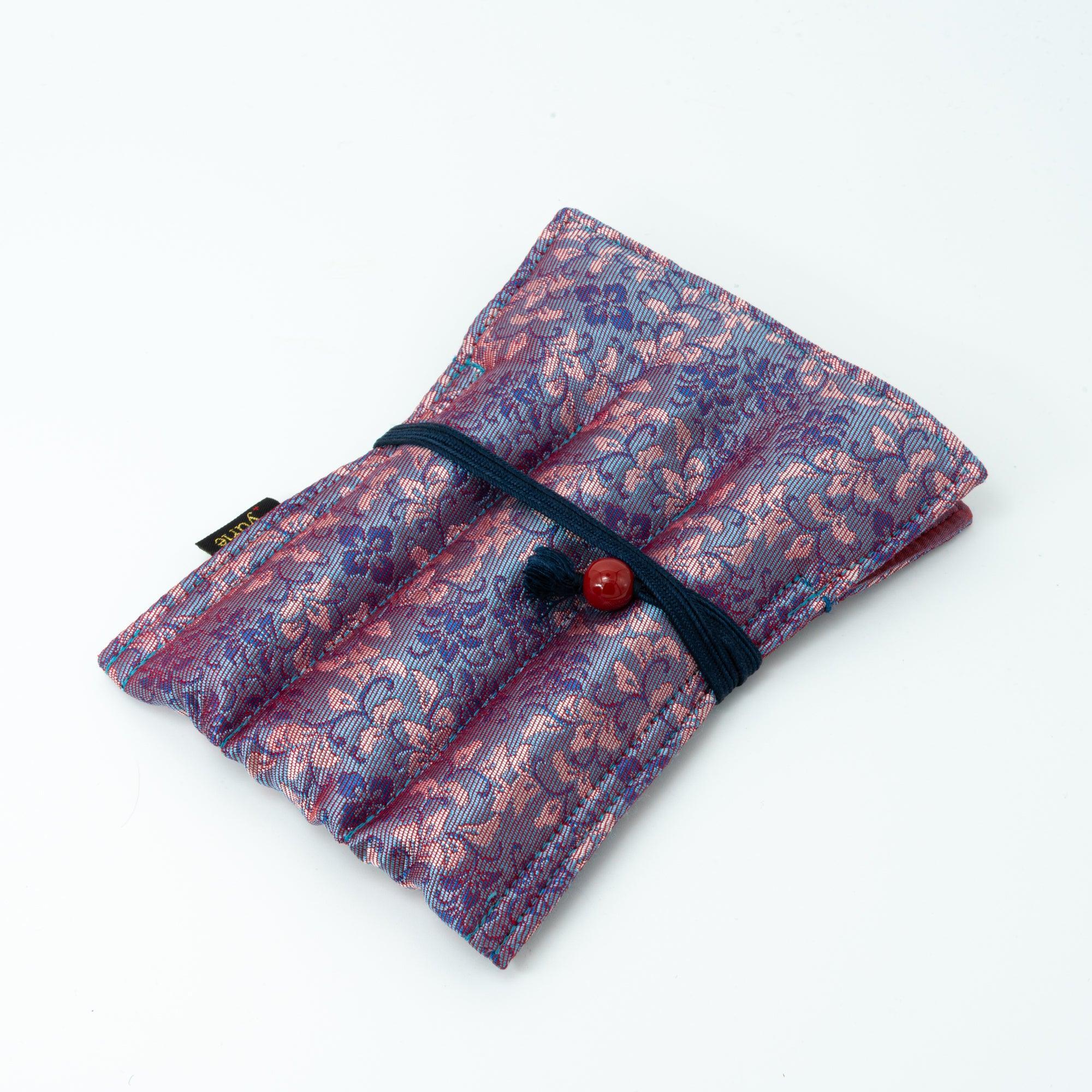 A compact Japanese fountain pen case made of Nishijin silk with pink and blue floral patterns, wrapped with a navy cord and red bead, displayed on a white background.