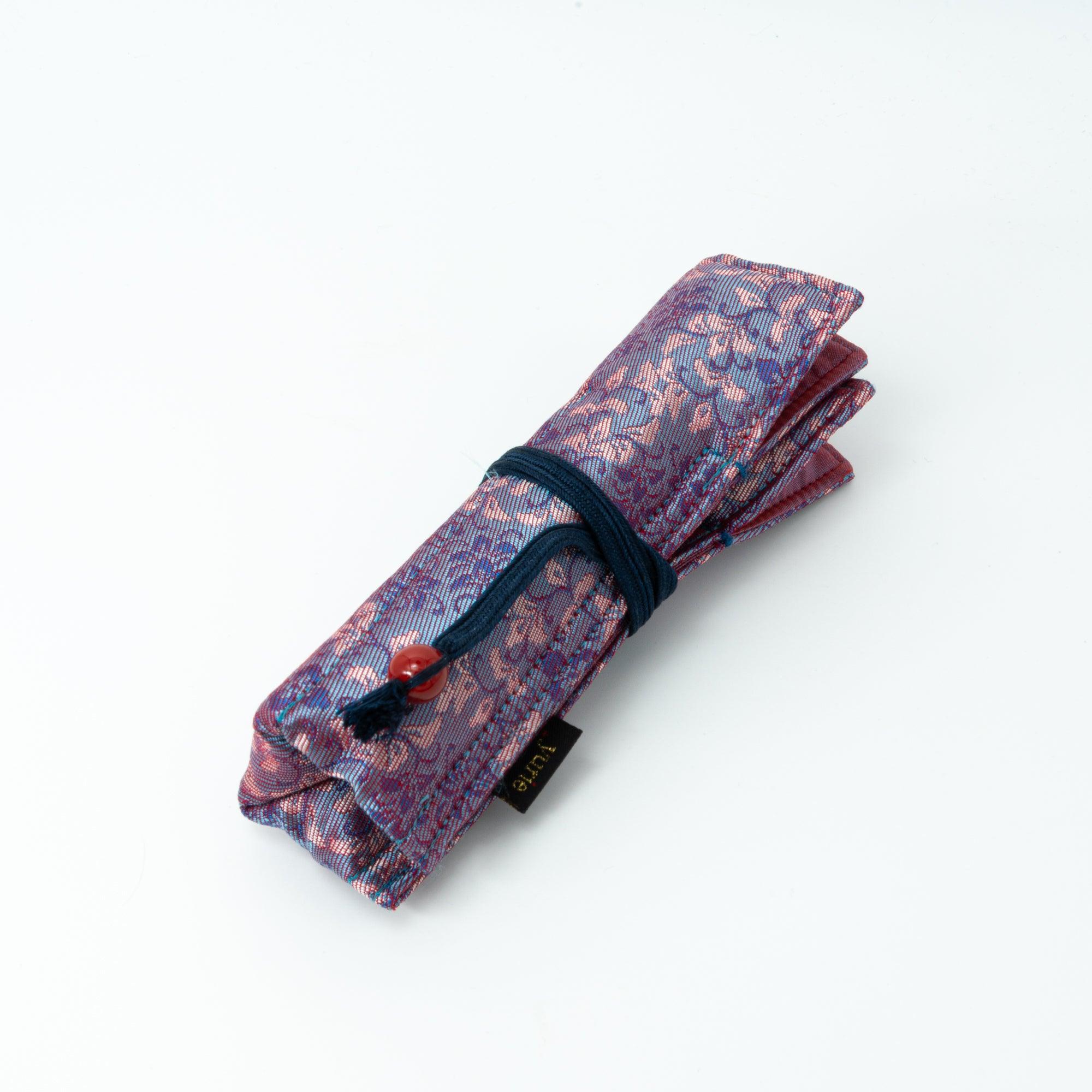 A Japanese fountain pen case in Nishijin silk with pink and blue floral patterns, featuring a navy cord and red bead, displayed flat against a white background.
