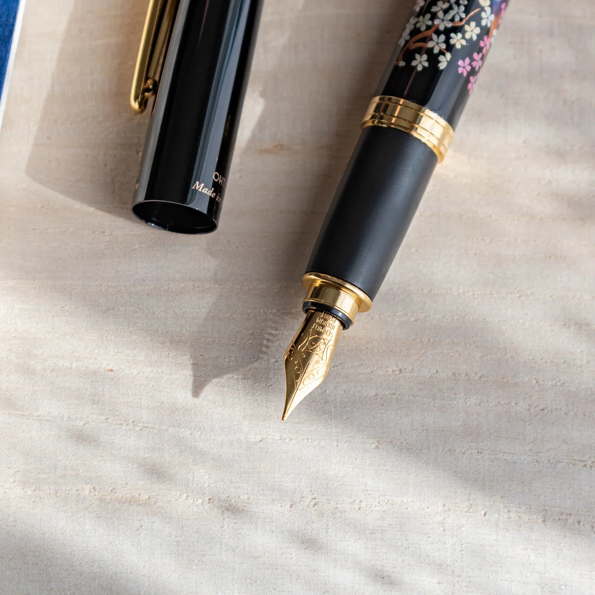 Close-up of a Japanese fountain pen with cherry blossoms and twilight Fuji artwork, showing its gold nib on a light desk.