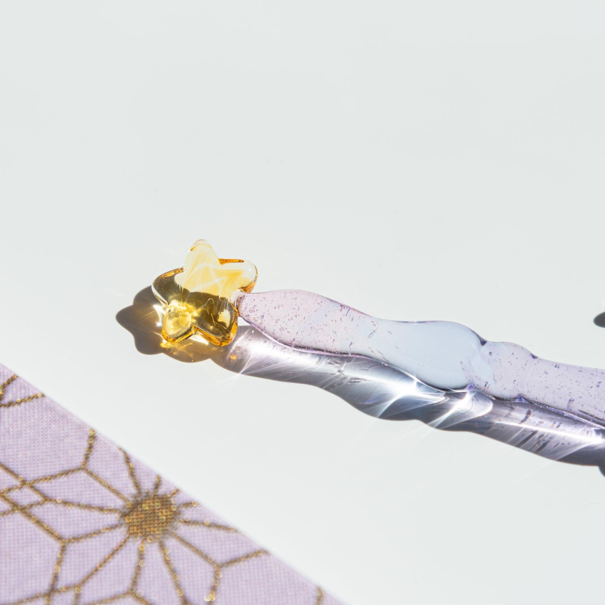 Close-up of the golden star top of a lavender glass pen. The transparent glass reflects light beautifully on a white surface.