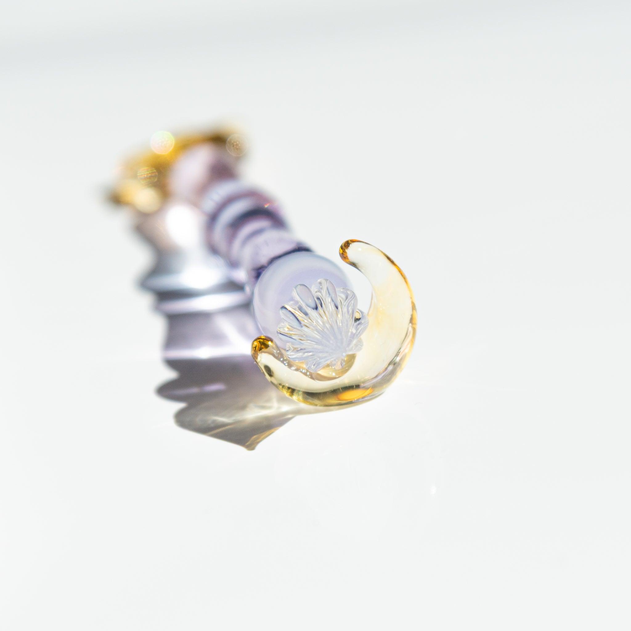 Extreme close-up of a lavender glass pen's nib, resting near a golden crescent moon pen rest, casting shimmering reflections.