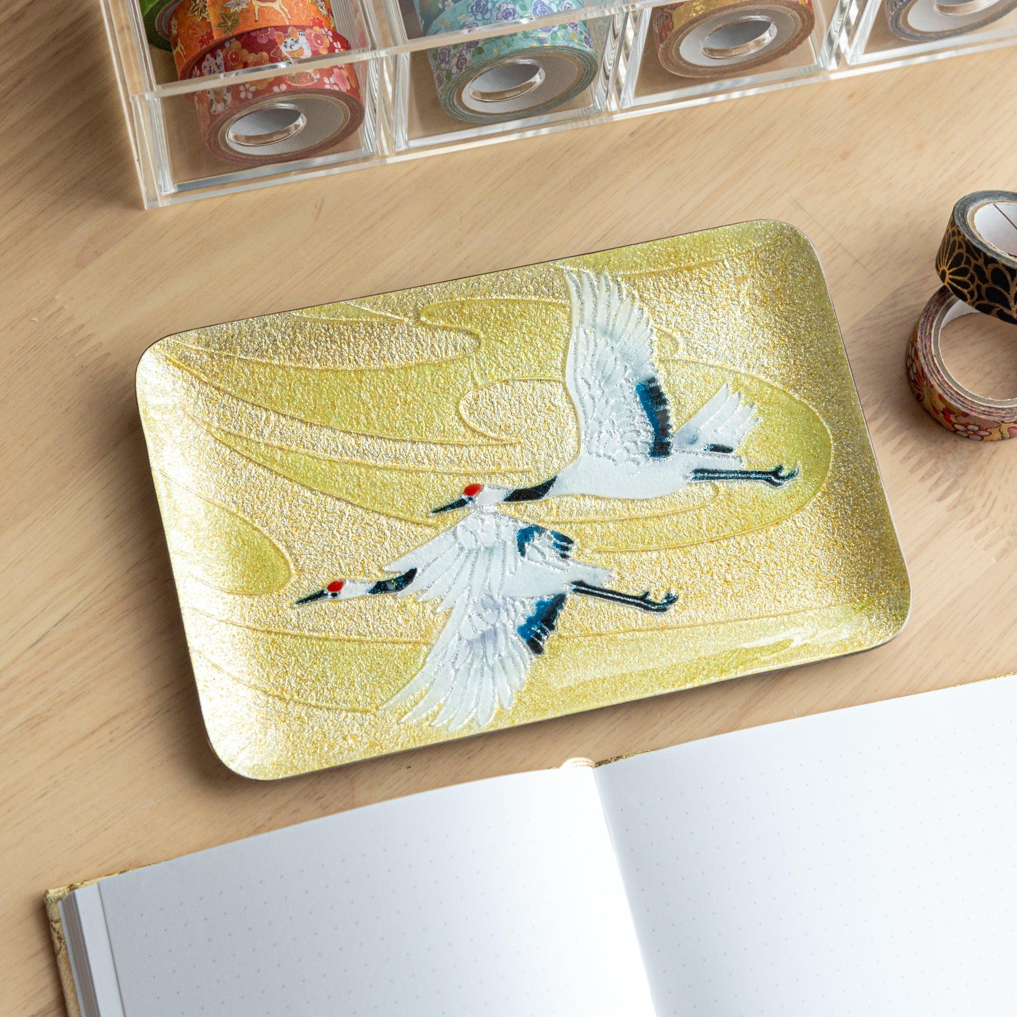 Japanese shippo ware pen tray with twin cranes in flight on gold, rounded rectangle, on wood desk with washi tape rolls