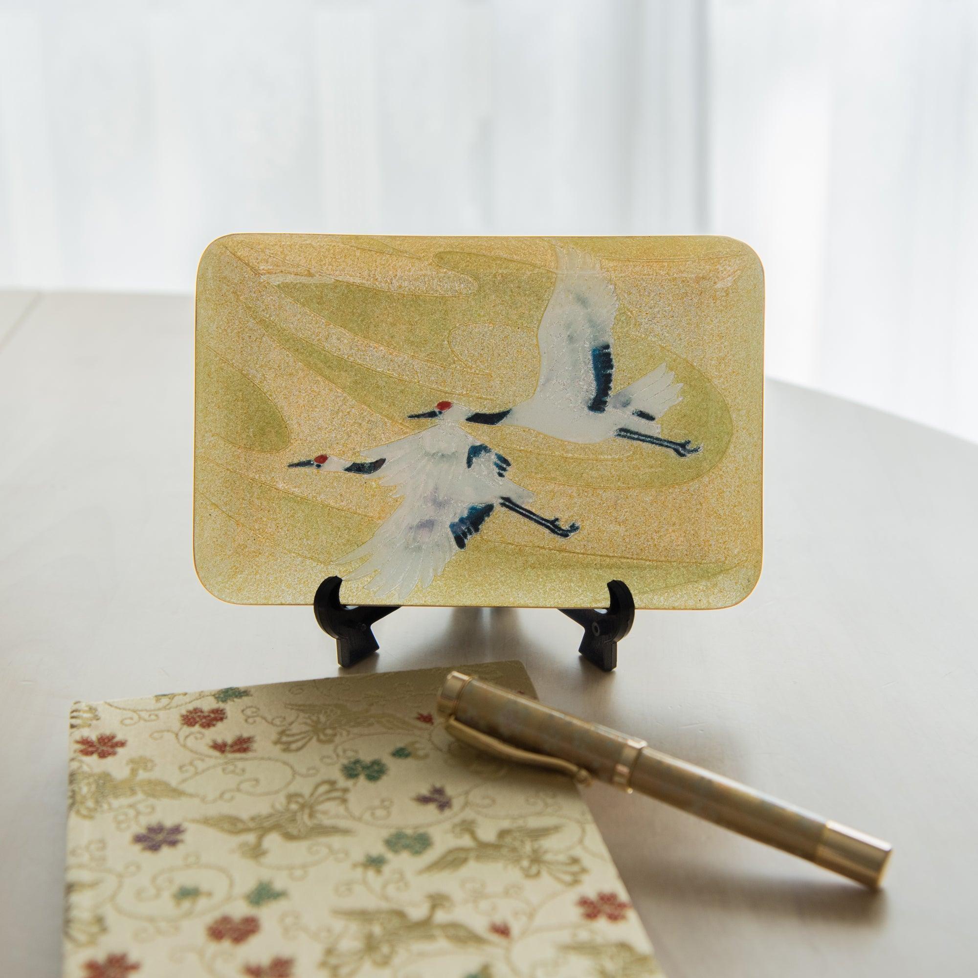 Japanese shippo ware pen tray with twin cranes on gold displayed on a black easel, floral notepad and gold pen below