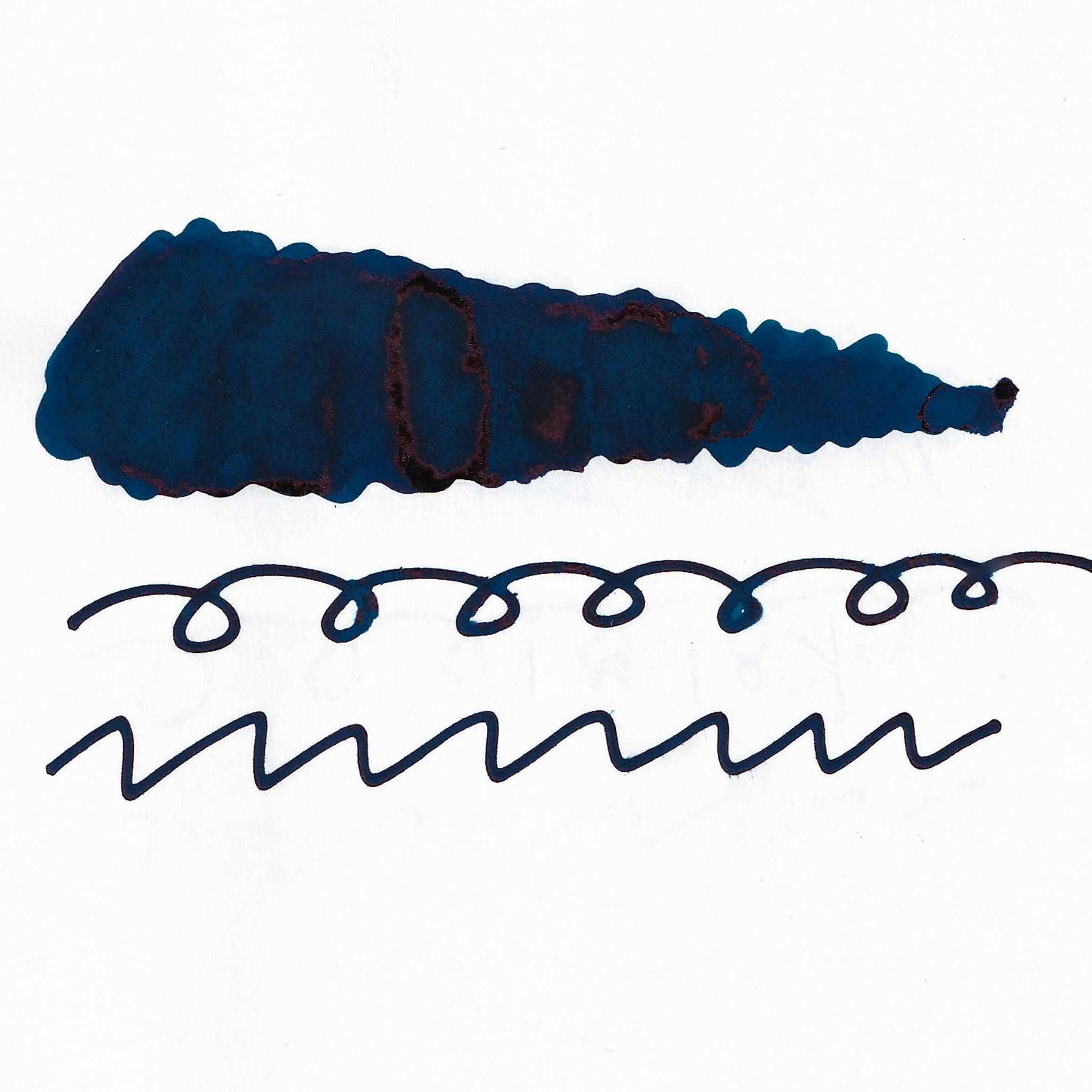 Swatch of deep blue fountain pen ink on white paper. The ink shows shading and sheen, with dark pooling and red undertones. Below are wavy and looped lines.