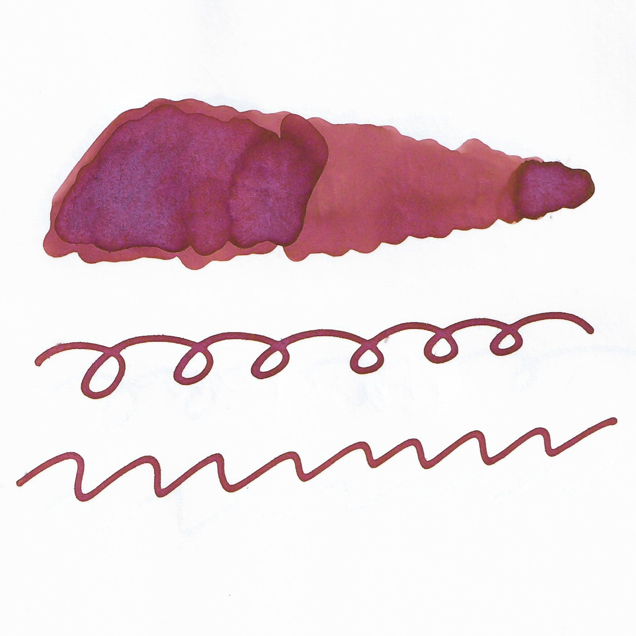 Swatch of reddish-brown fountain pen ink on white paper. The ink shows shading variations, with a dark center and lighter edges. Below are wavy and looped lines demonstrating the ink's flow.