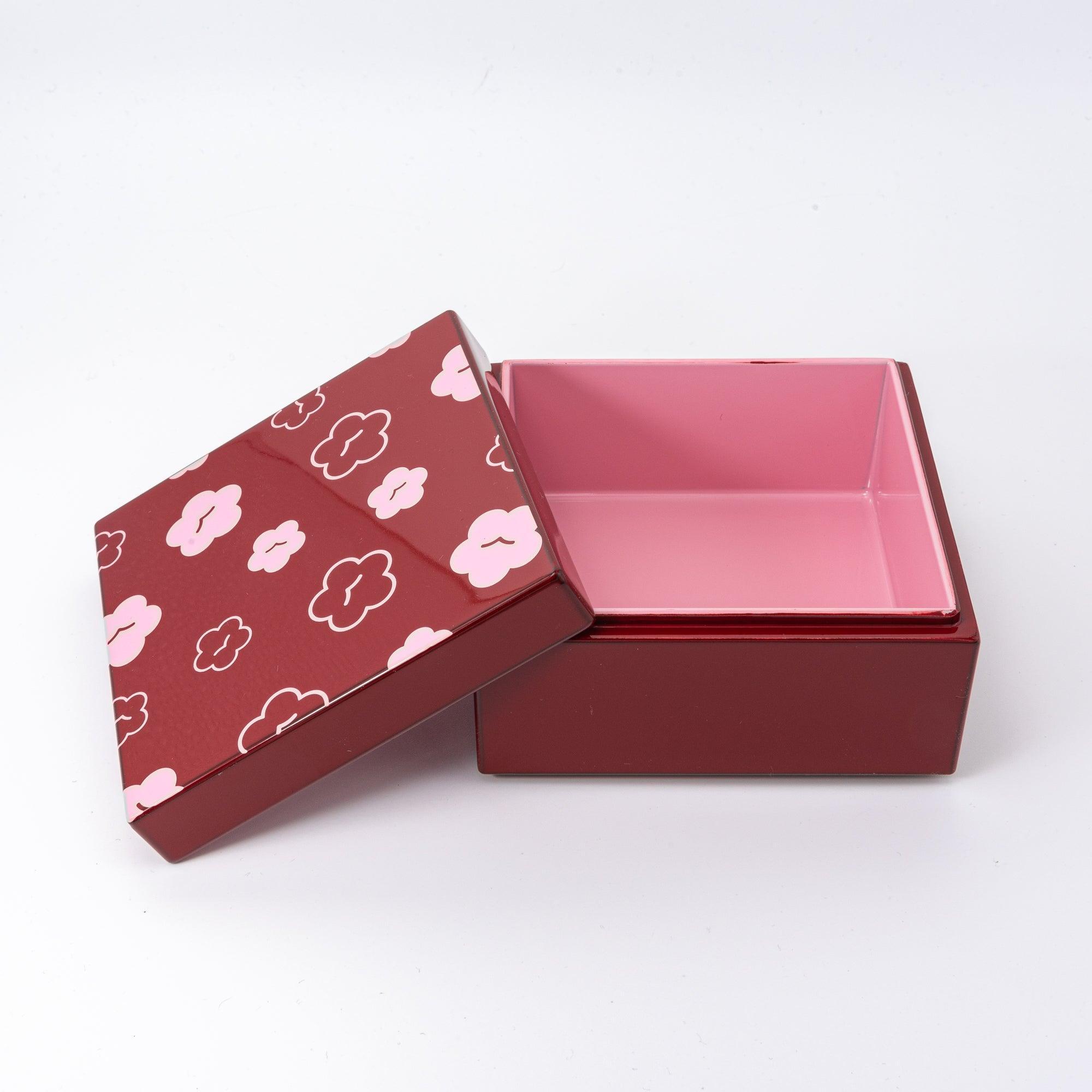 Open red Japanese lacquer stationery box with pink plum blossom patterns and a light pink interior, displayed on a white background with its lid slightly tilted.