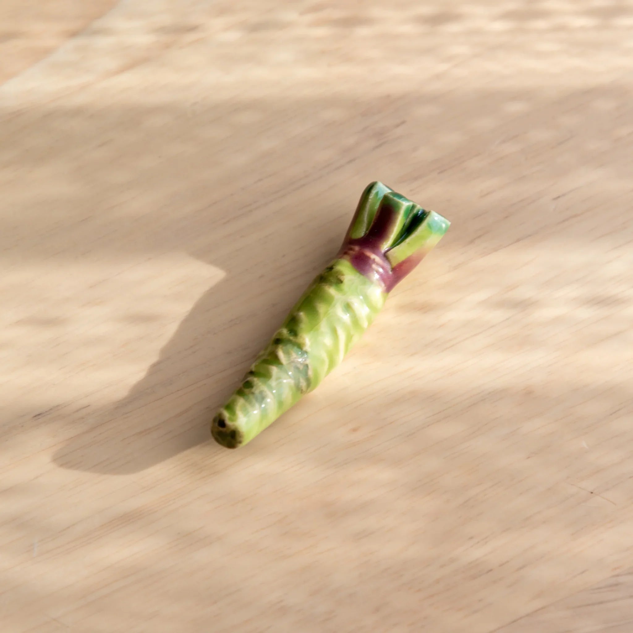 Vibrant green wasabi handcrafted pen rest with distinctive bumpy surface and functional grooved holder on neutral surface