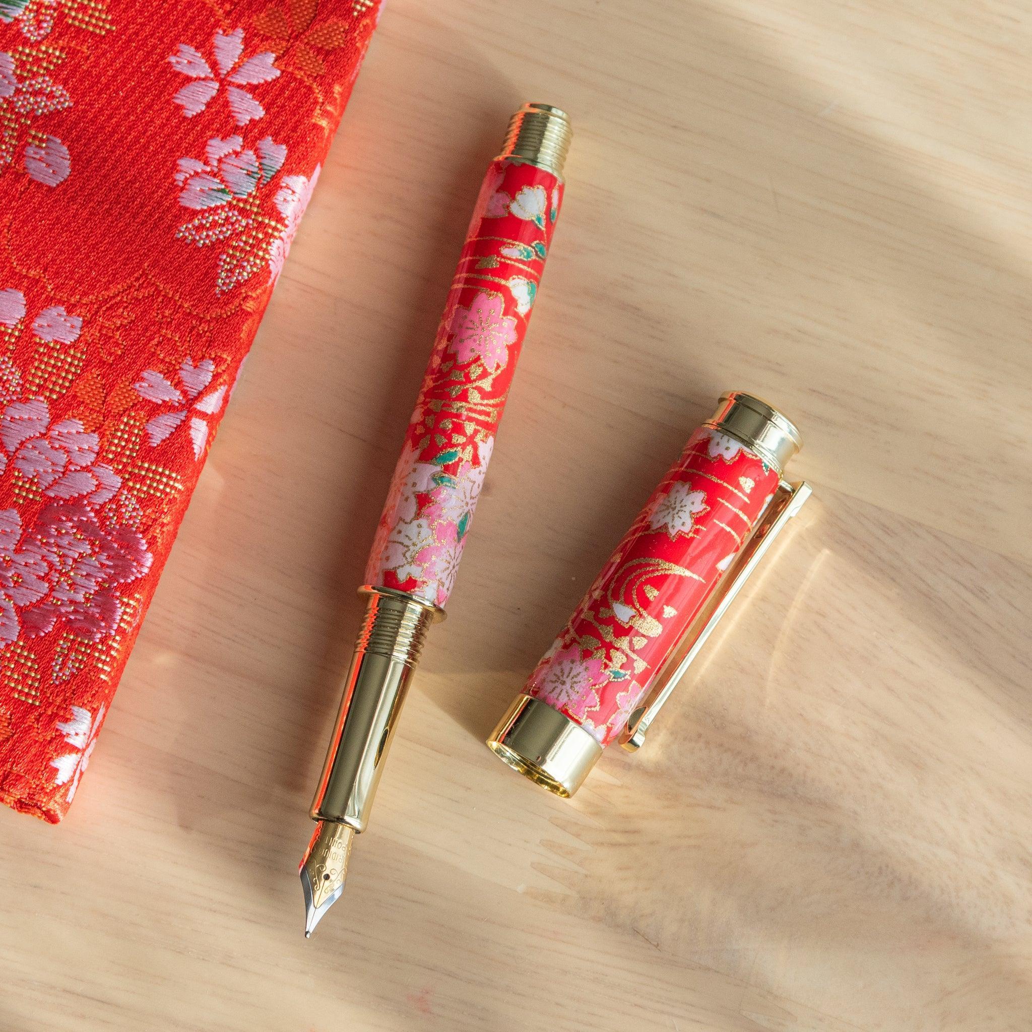 A red floral Japanese stationery fountain pen disassembled on a table with matching fabric beside it.