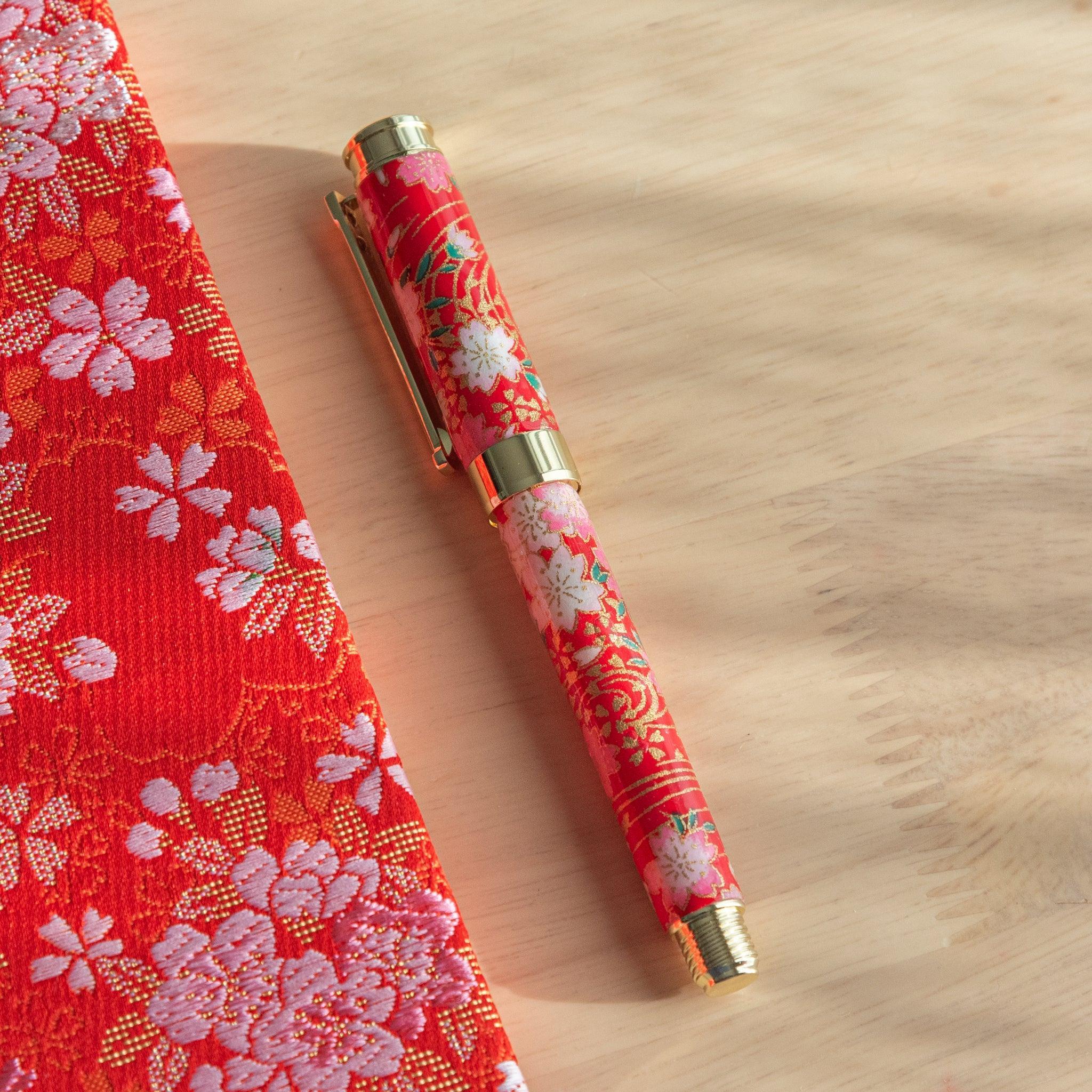 A red floral Japanese stationery fountain pen placed next to matching fabric under sunlight.