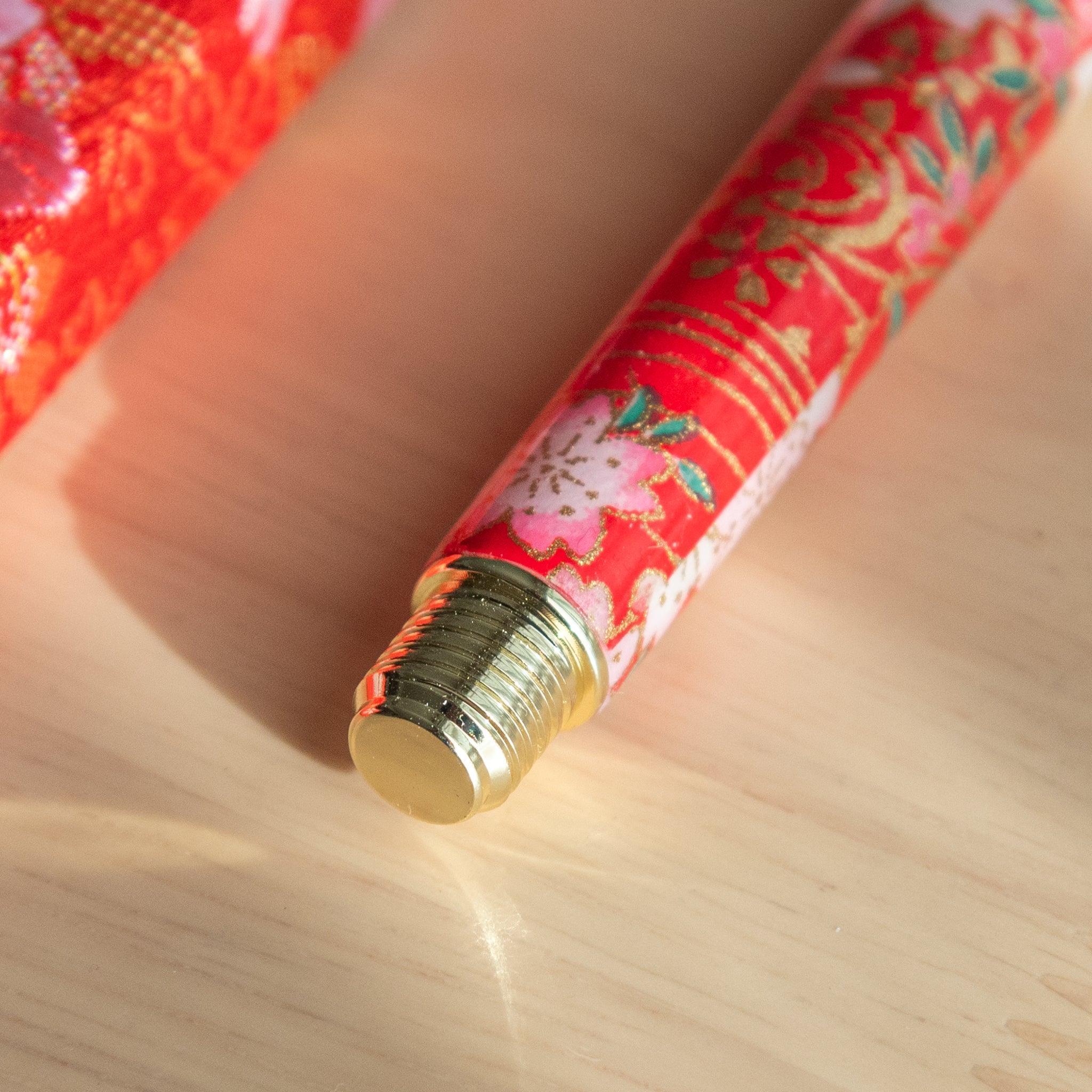 A close-up of the bottom cap of a red floral Japanese stationery fountain pen with gold accents.