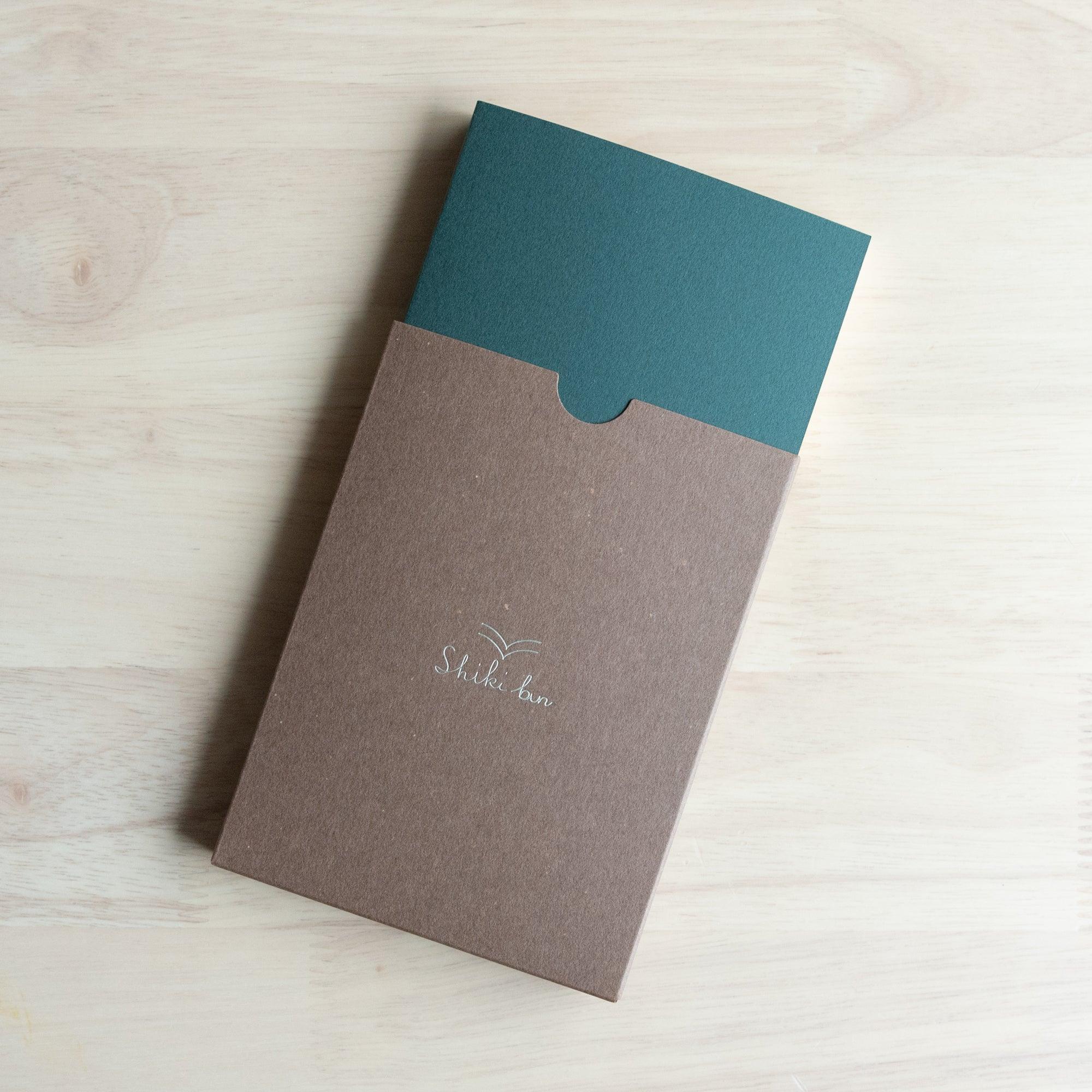 Wooden Page Softcover Notebook A6 in deep green sliding out of Shiki-bun package - traditional Japanese design