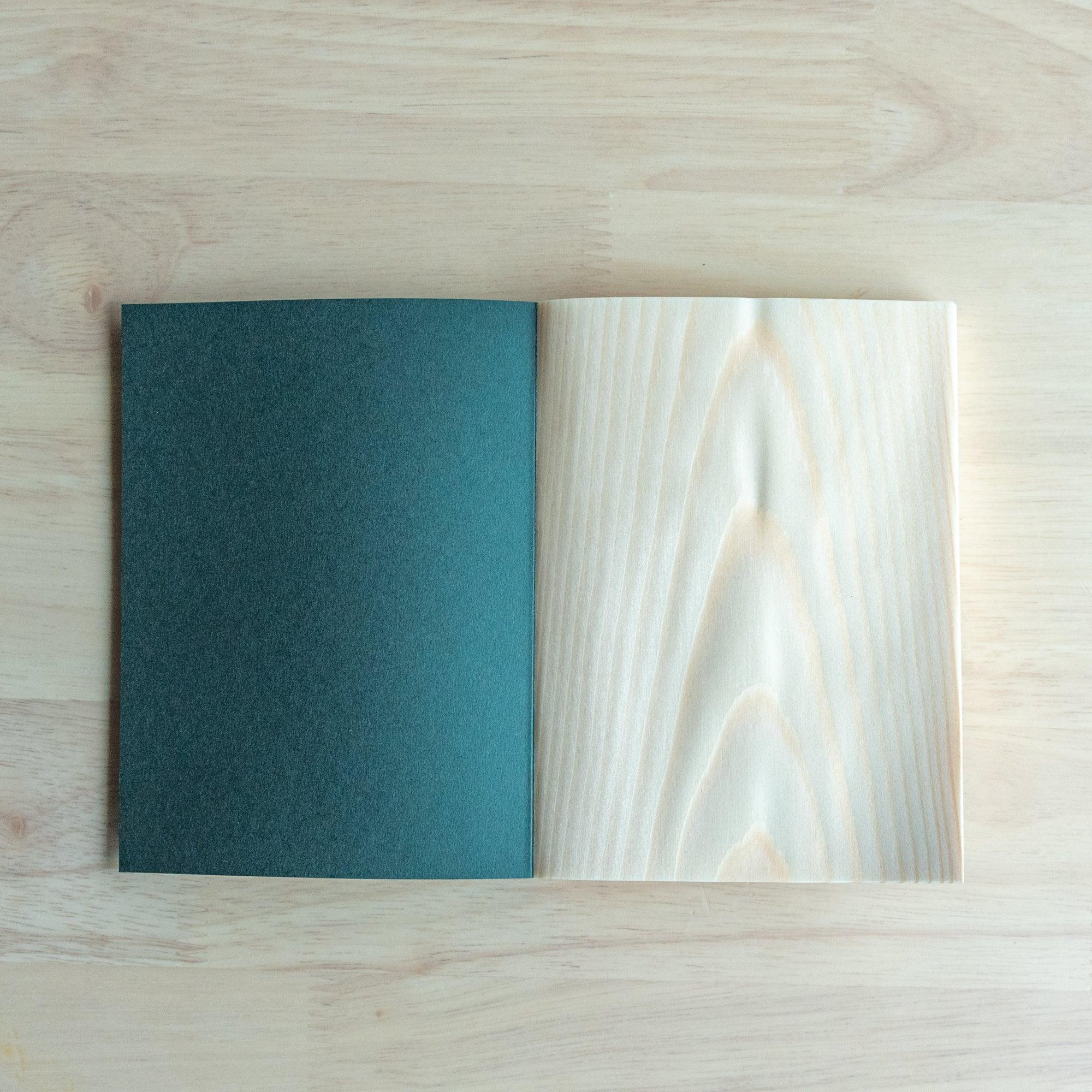 Wooden Page A6 Notebook open revealing textured red pine wood pages and minimalist deep green cover