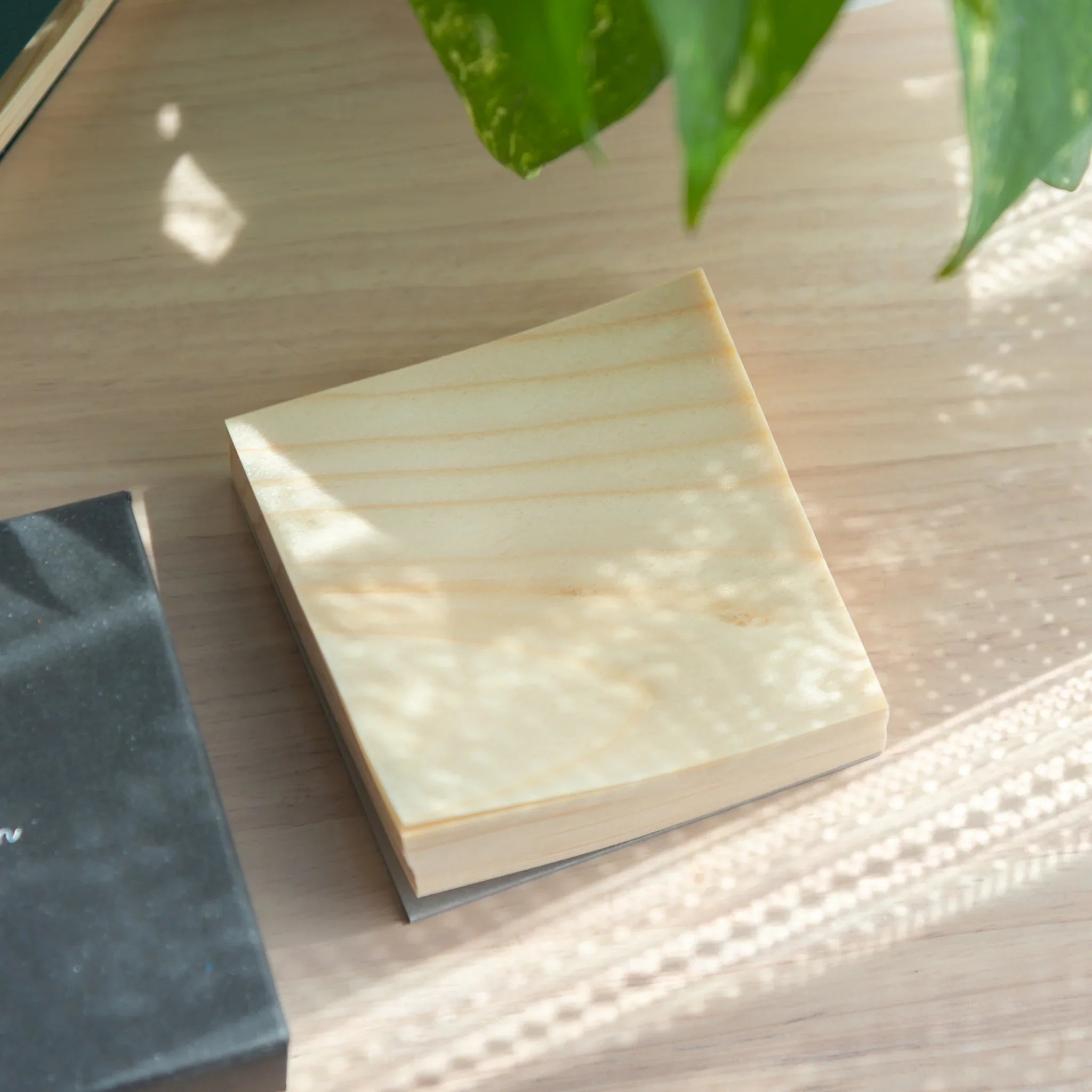 Stack of Japanese wooden sheet memo pad on light wood surface showing natural wood grain top sheet and slim profile