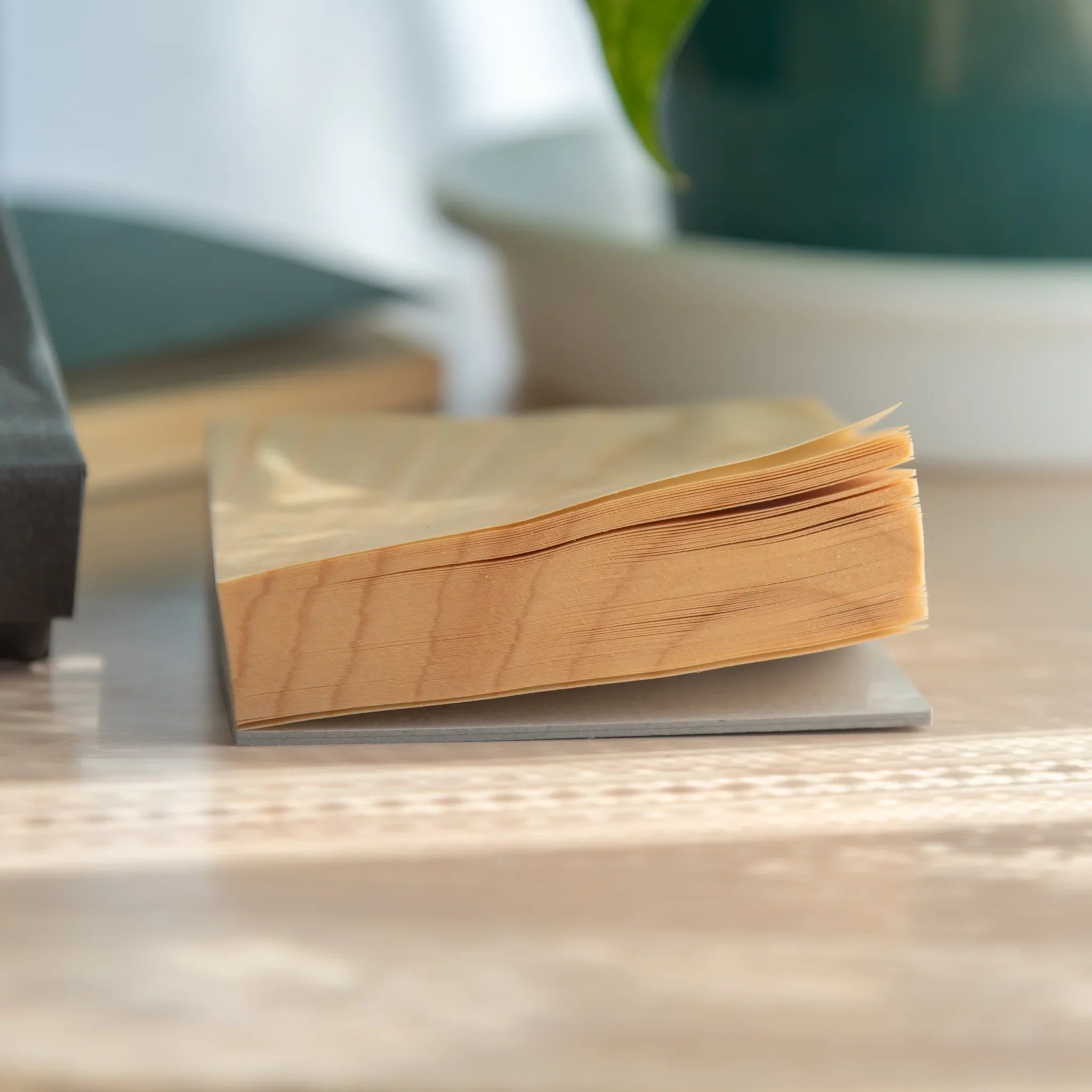 Side profile of Japanese wooden sheet memo pad showing stack of thin wood veneer sheets on grey cardboard base