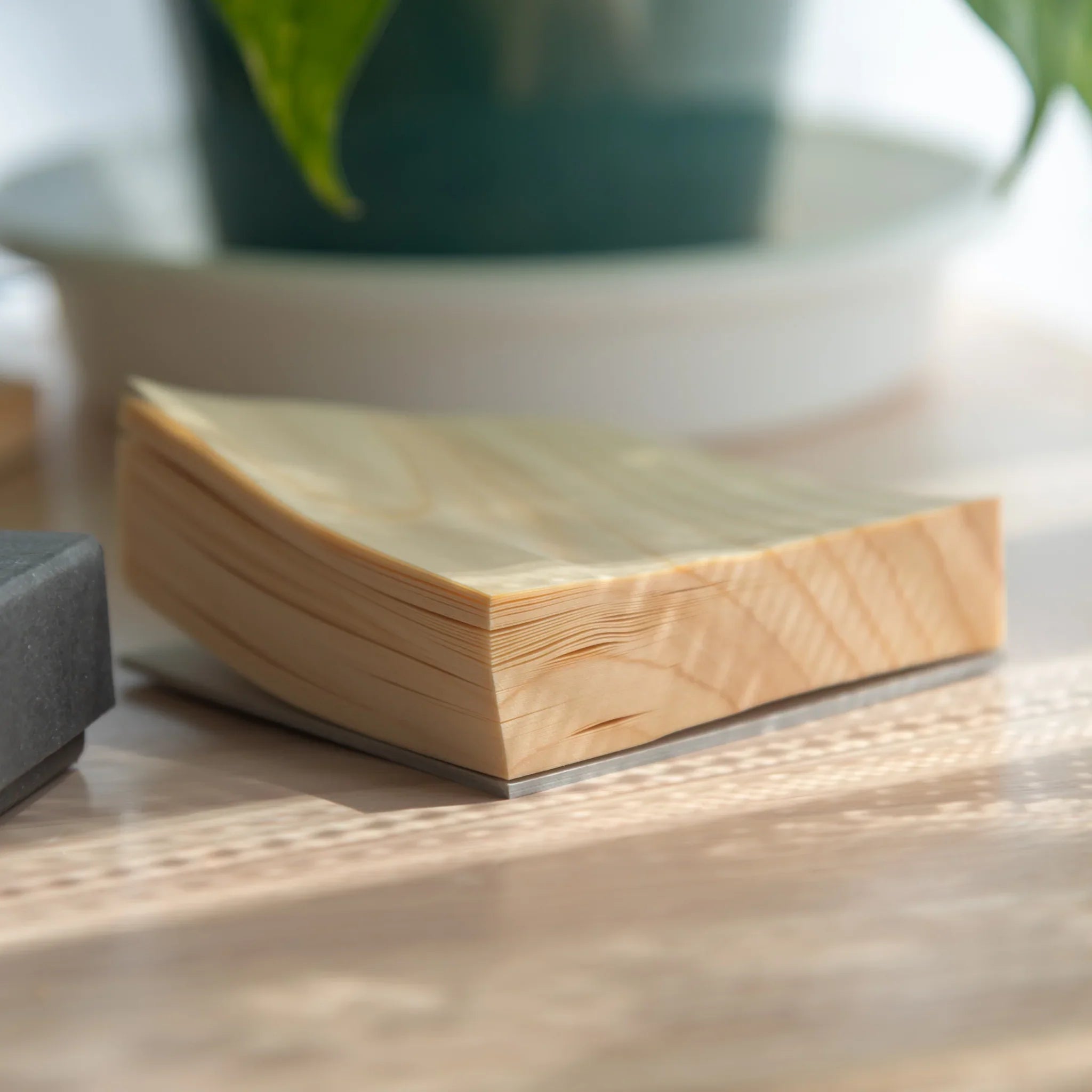 Close-up corner view of Japanese wooden sheet memo pad showing stack of natural grain wood veneer sheets on metal backing